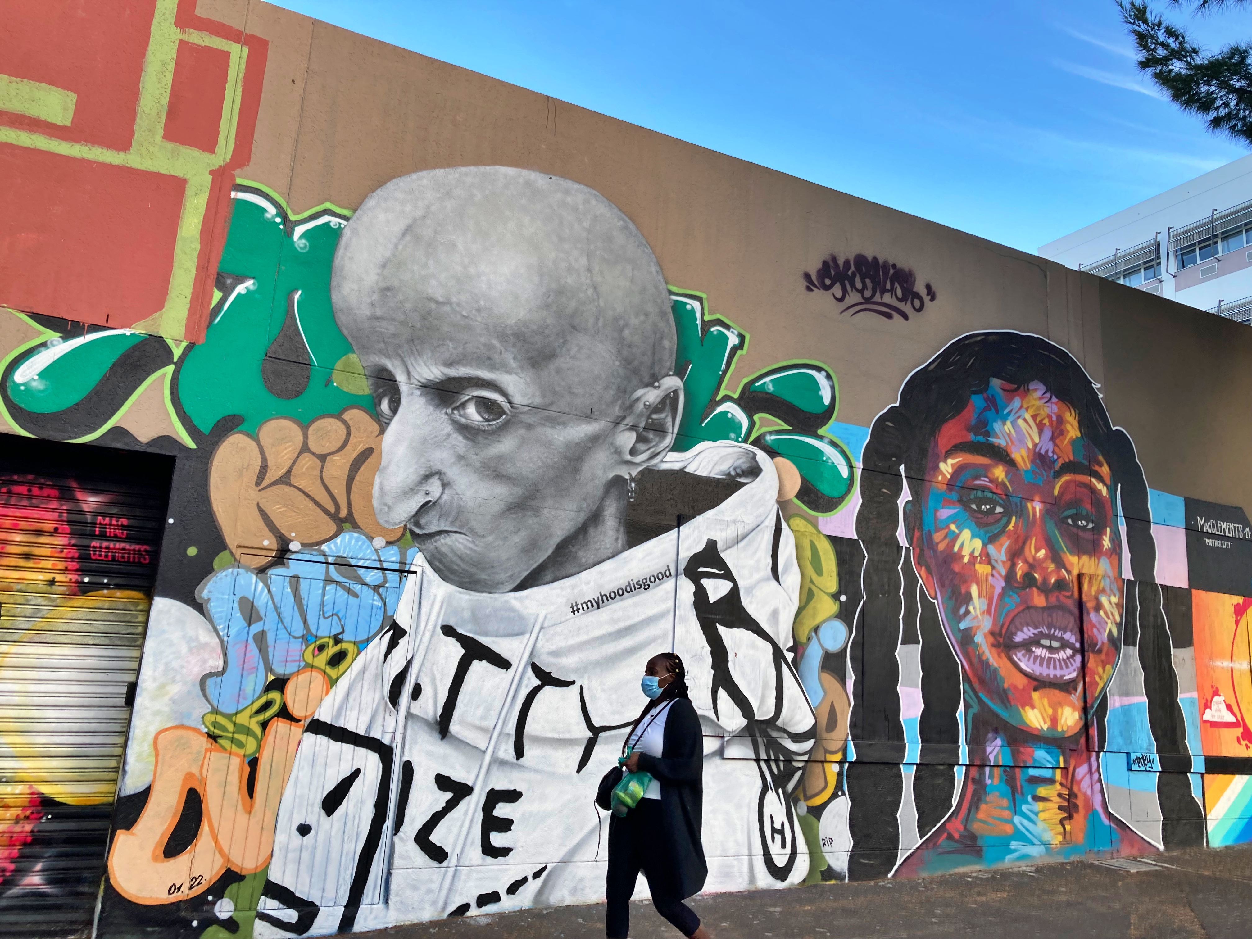 A woman in a mask walks past street art in Cape Town, South Africa