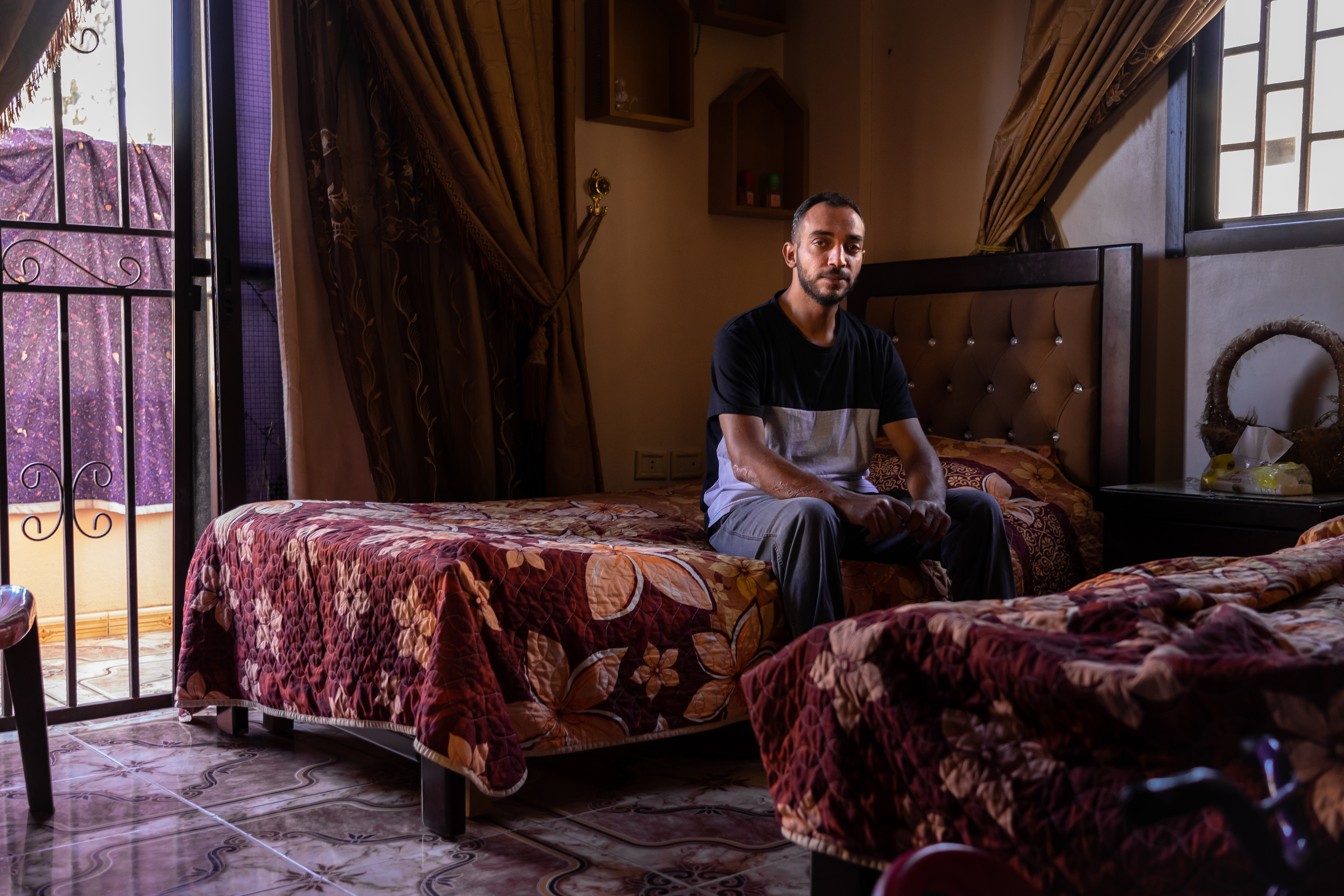 A man sits alone on a bed in a darkened room 