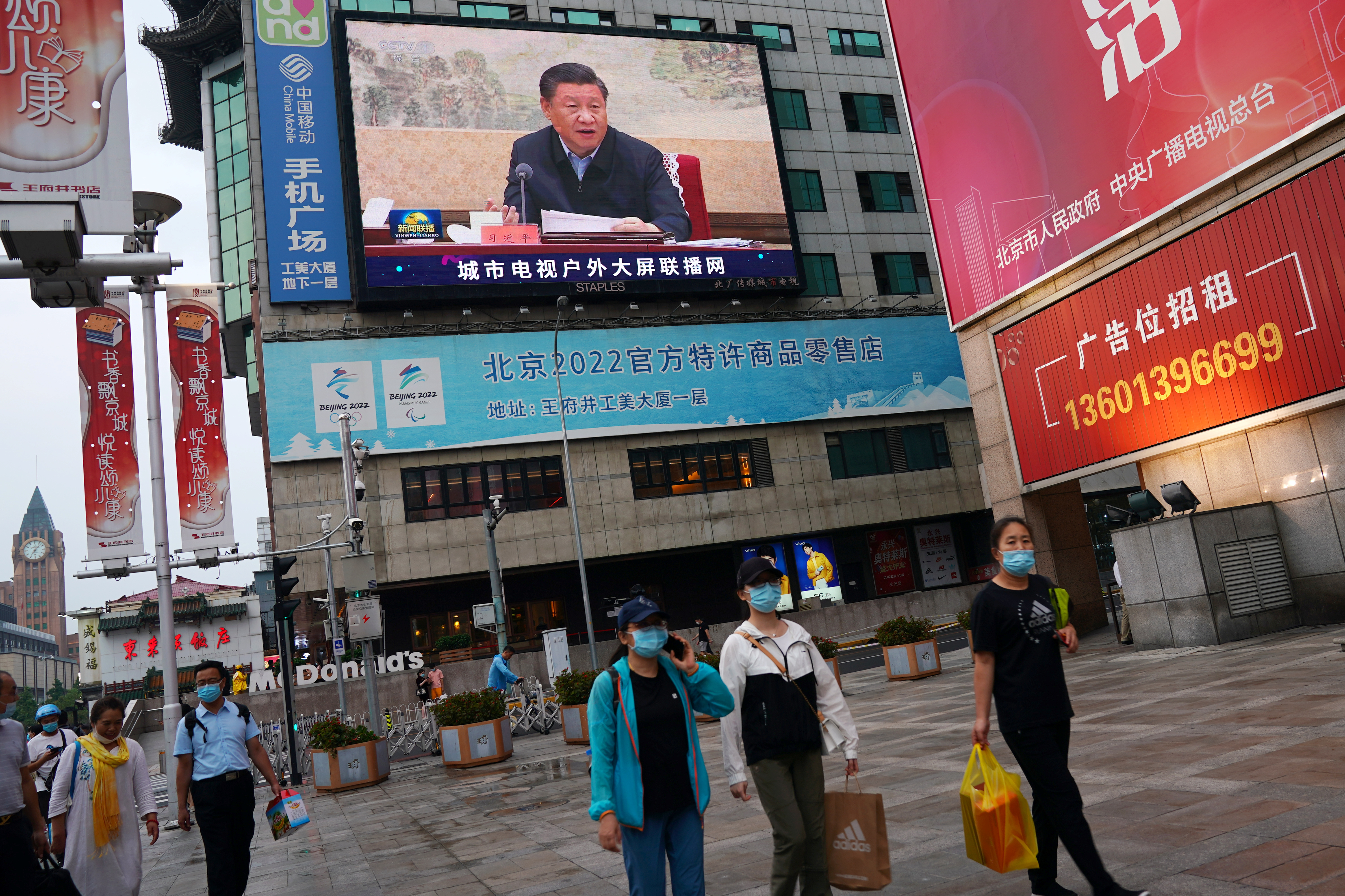 People walk near a screen showing Chinese President Xi Jinping