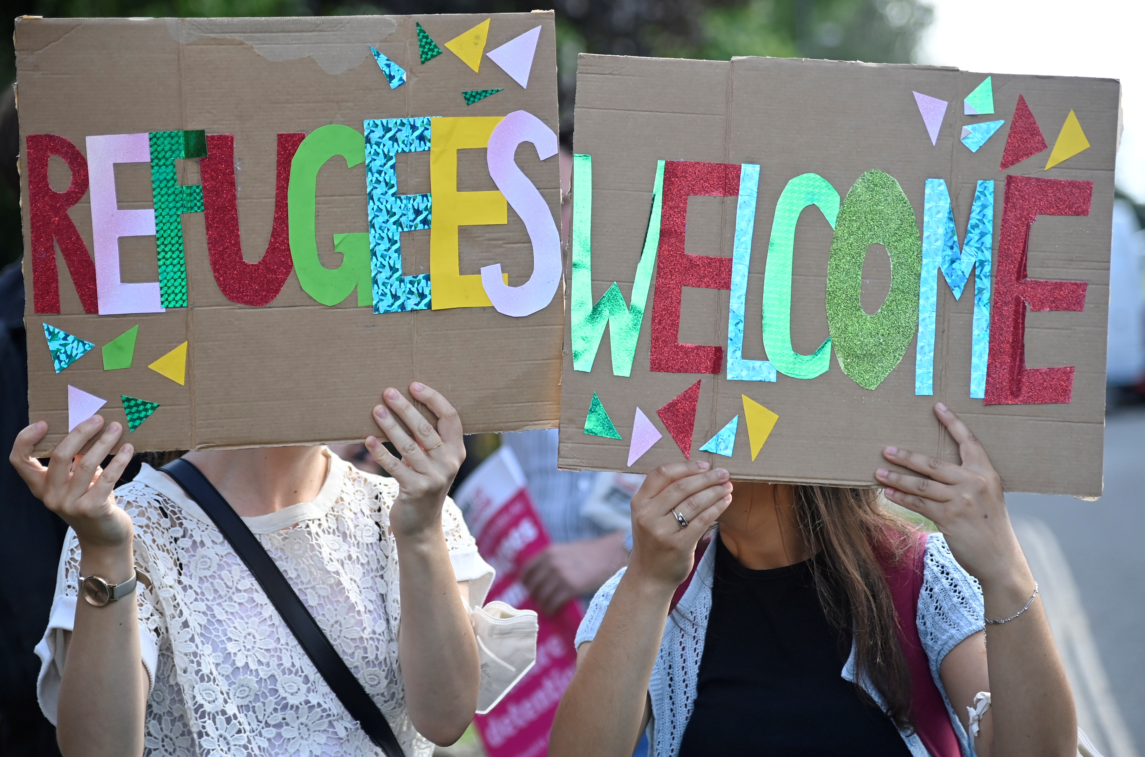 Two women hold up signs in bright colours reading 'refugees welcome'