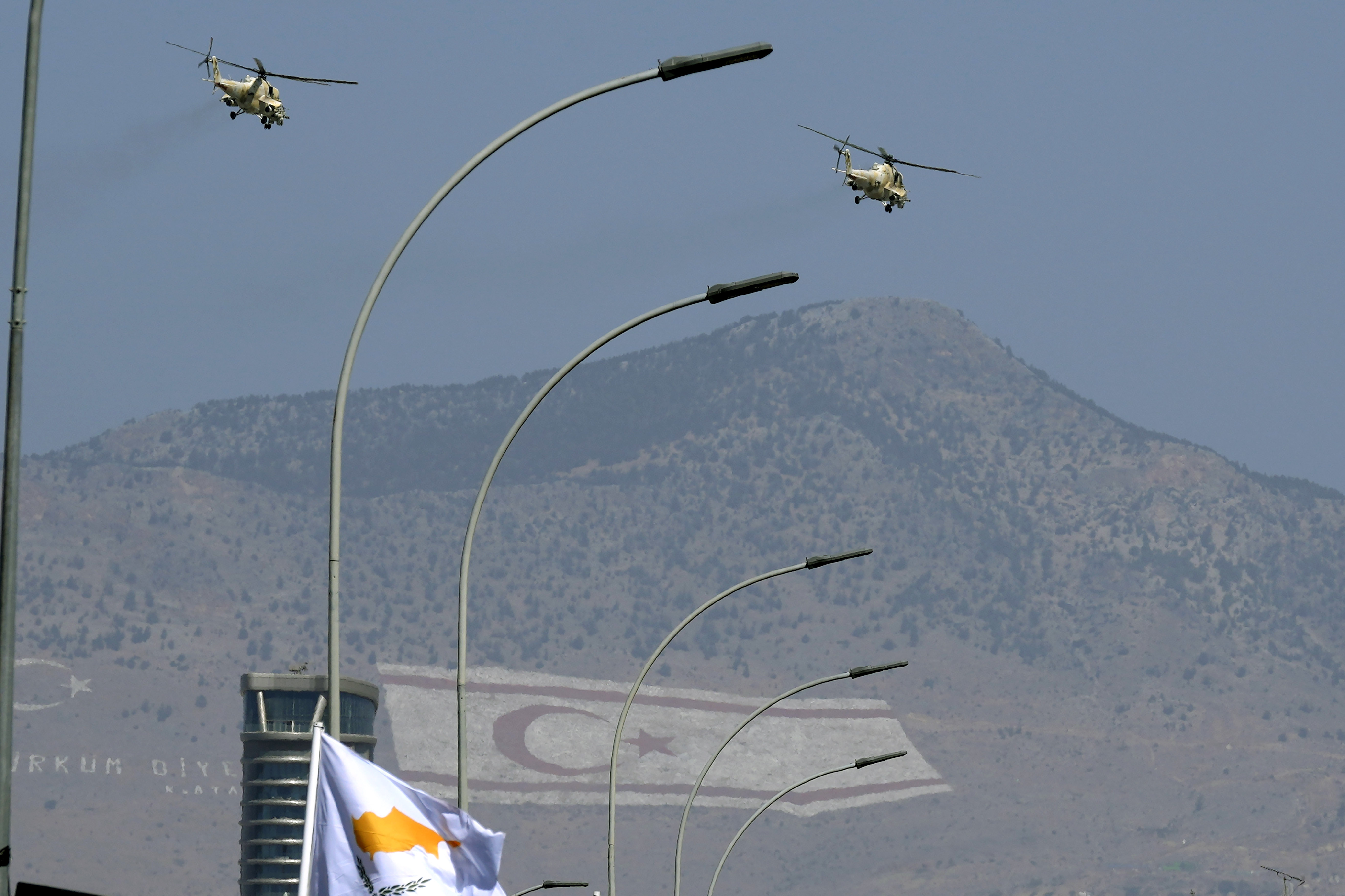 Military helicopters of Cypriot air forces fly over a military parade marking the 62nd anniversary of Cyprus' independence from British colonial rule, as the giant paintings of the Turkish and the Turkish Cypriot breakaway flags are seen on Pentadahtilos mountain in the Turkish occupied area in the background, in Nicosia, Cyprus