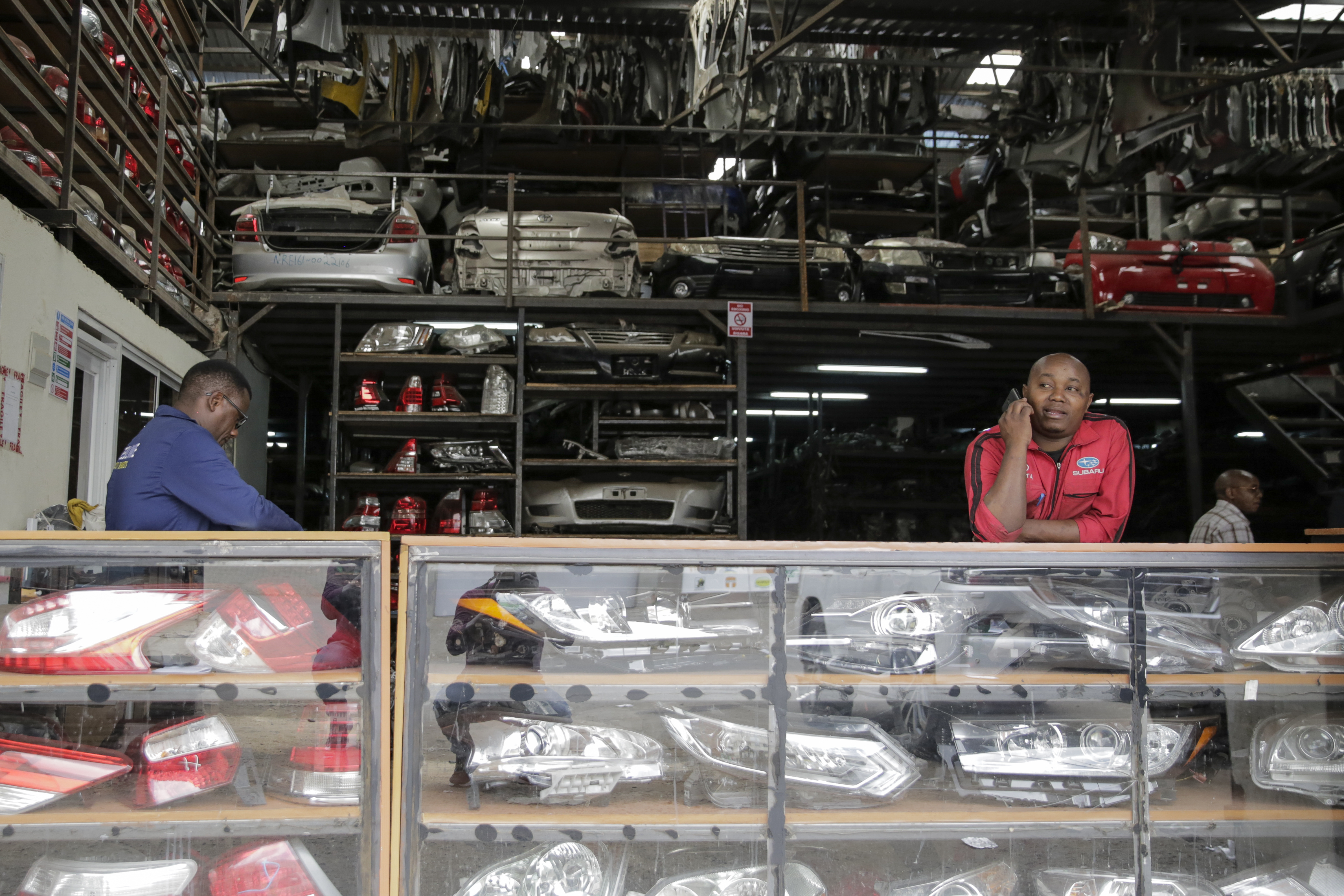 Salesmen wait for customers at a secondhand car parts warehouse, with car parts behind them and on display in the counter, in the industrial area of the capital Nairobi, Kenya