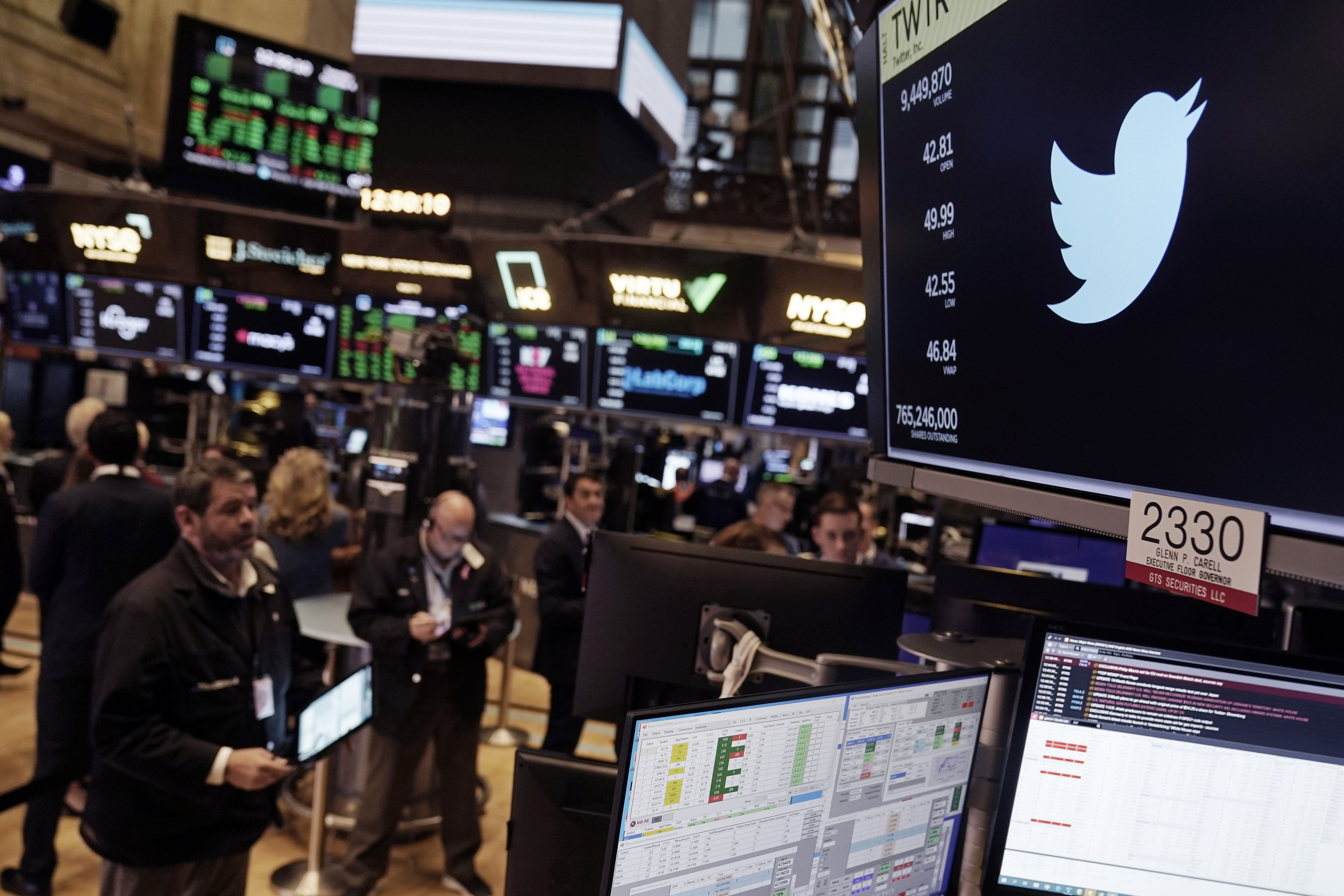 The symbol for Twitter appears above a trading post on the floor of the New York Stock Exchange as brokers take notes.