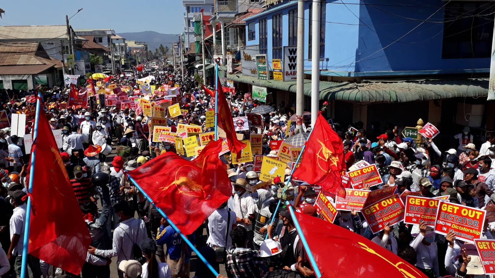 Crowds of people march through a street in Launglone in September with red flags and placards reading 'Get out dictator. End the dictatorship in Myanmar'.