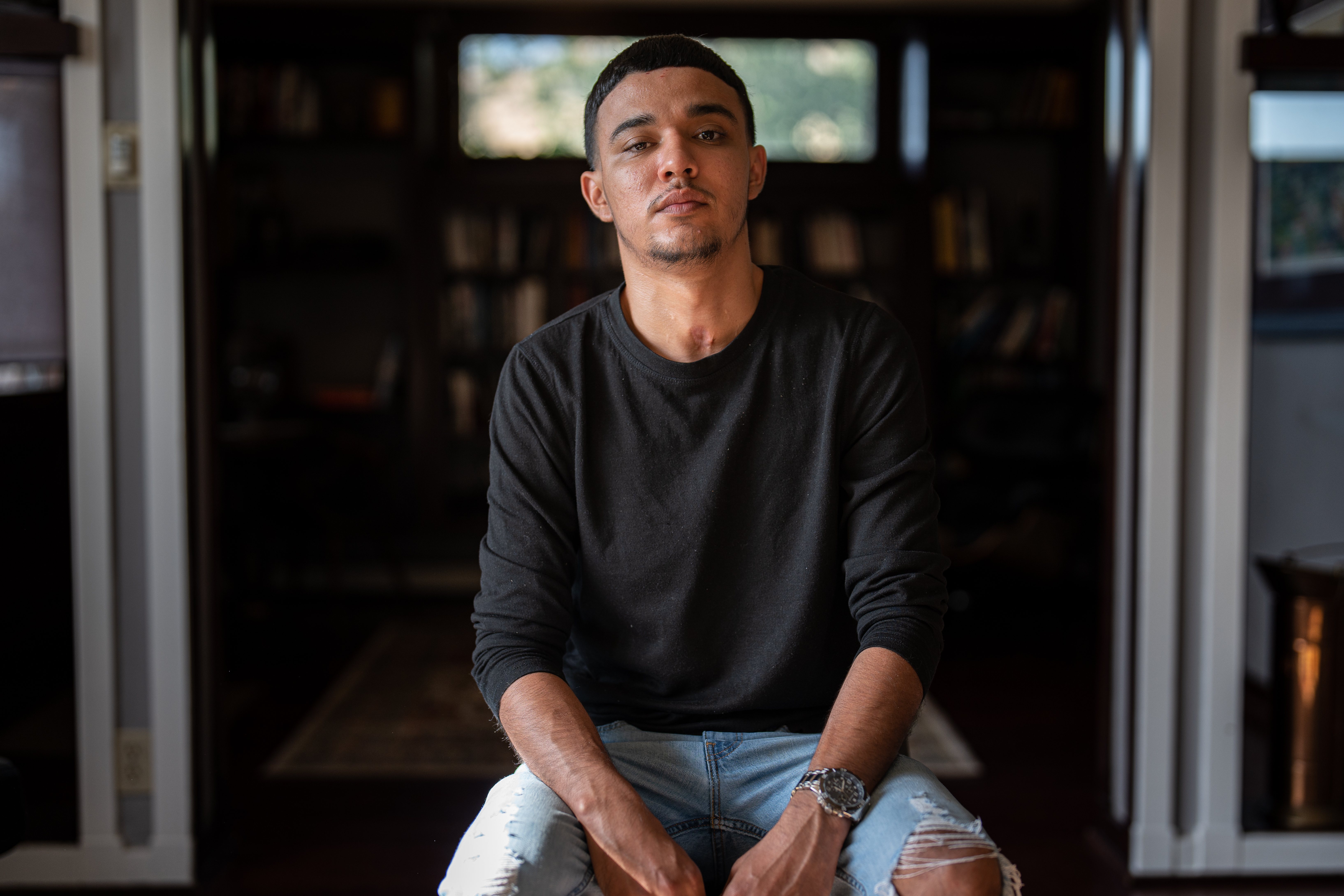 A photo of a person sitting in a chair indoors in front of the camera, looking towards the camera taking a photo of them.