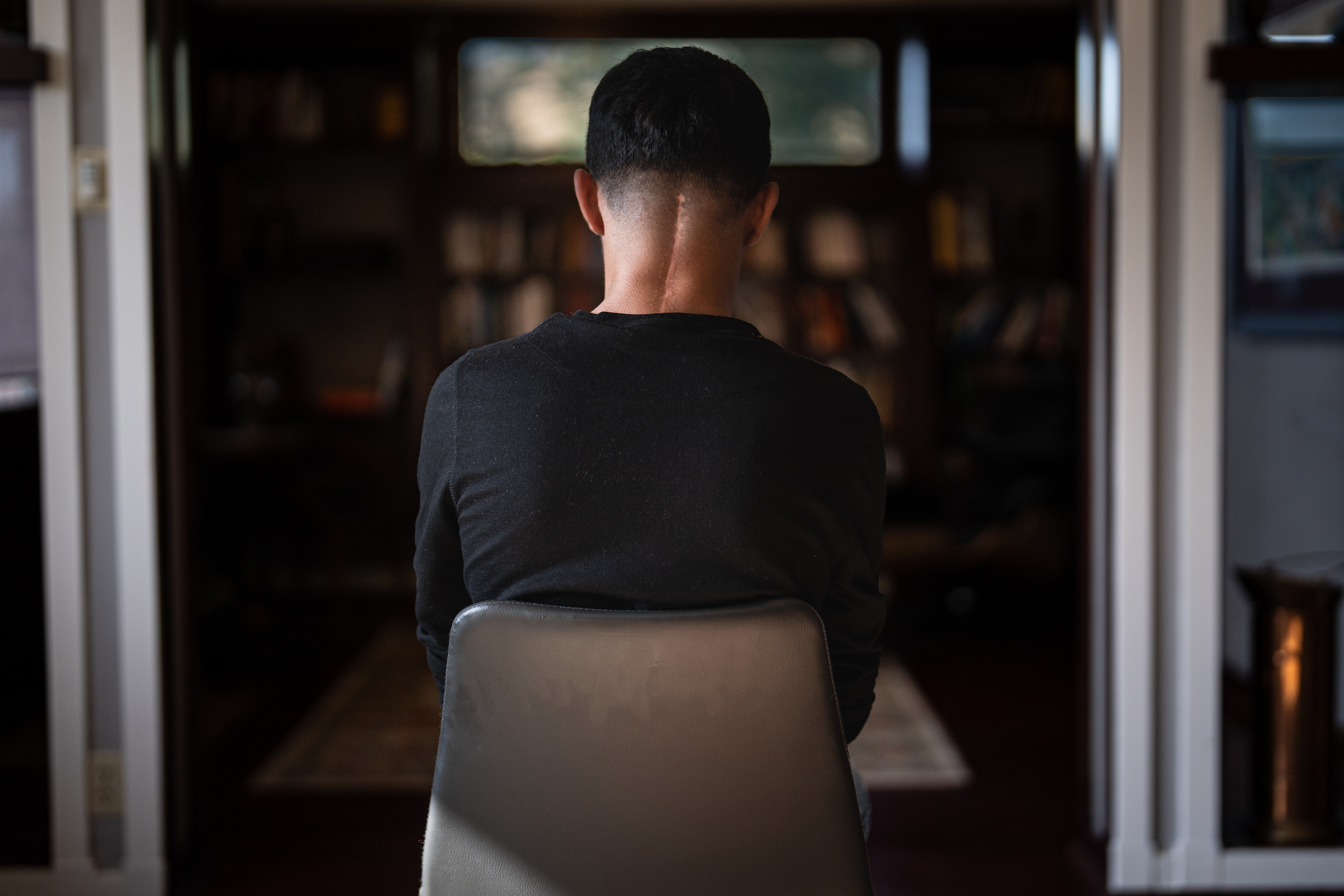 A photo of a person sitting in a chair indoors with their back facing the camera taking a photo of them.