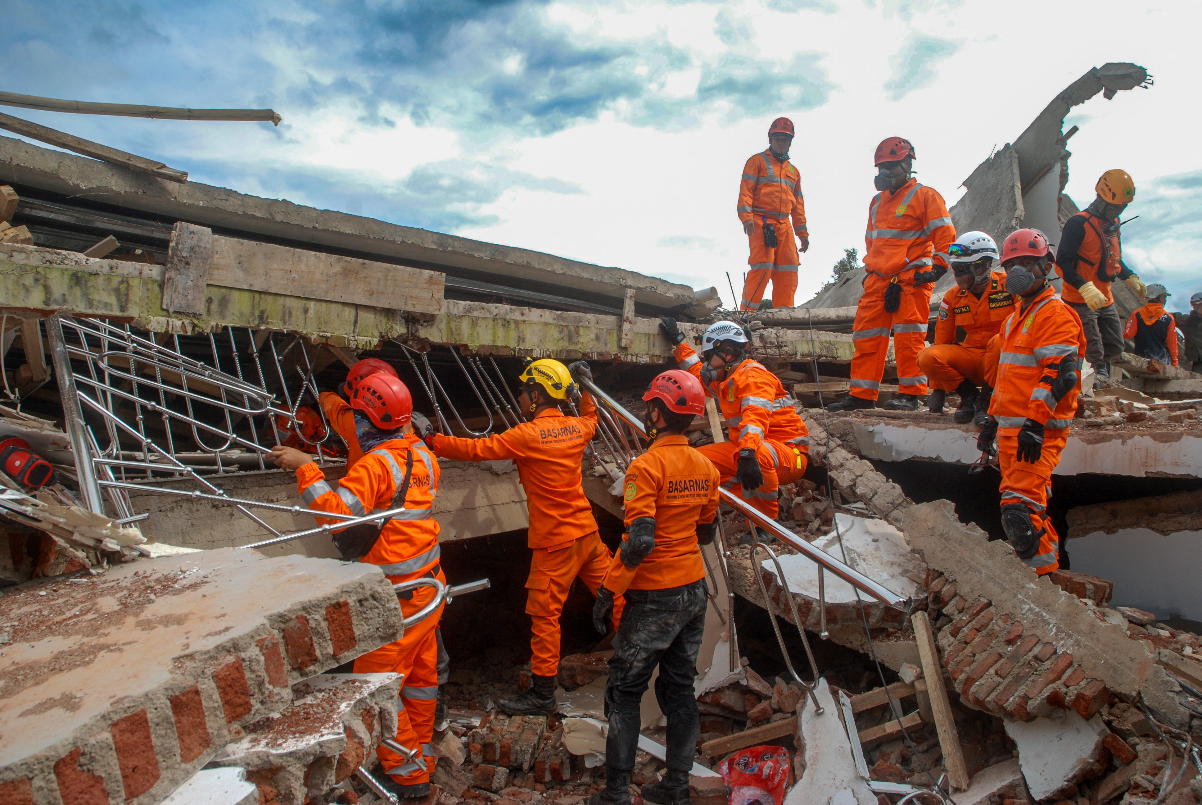 Rescuers in orange uniforms standing on front of an on top of a collapsed building