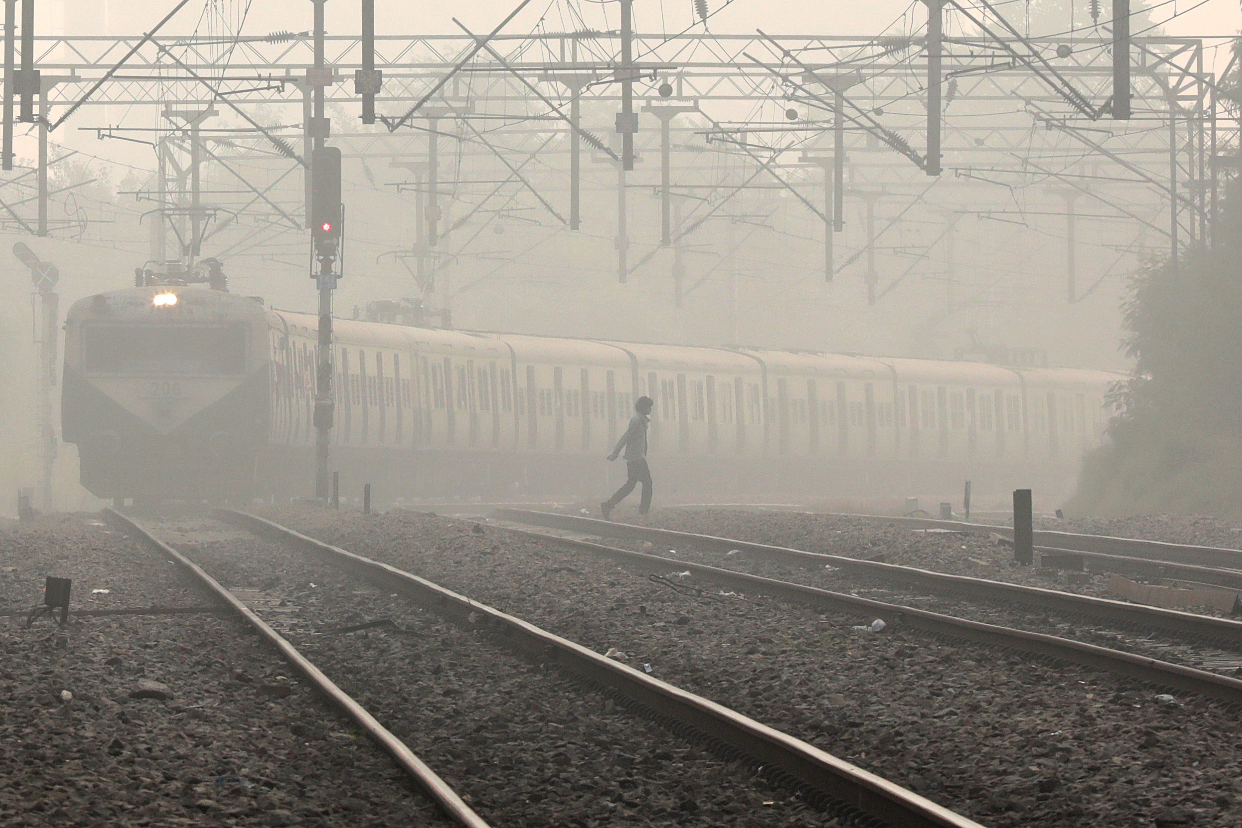 A train moves as a daily commuter walks through a railway track near a railway station.