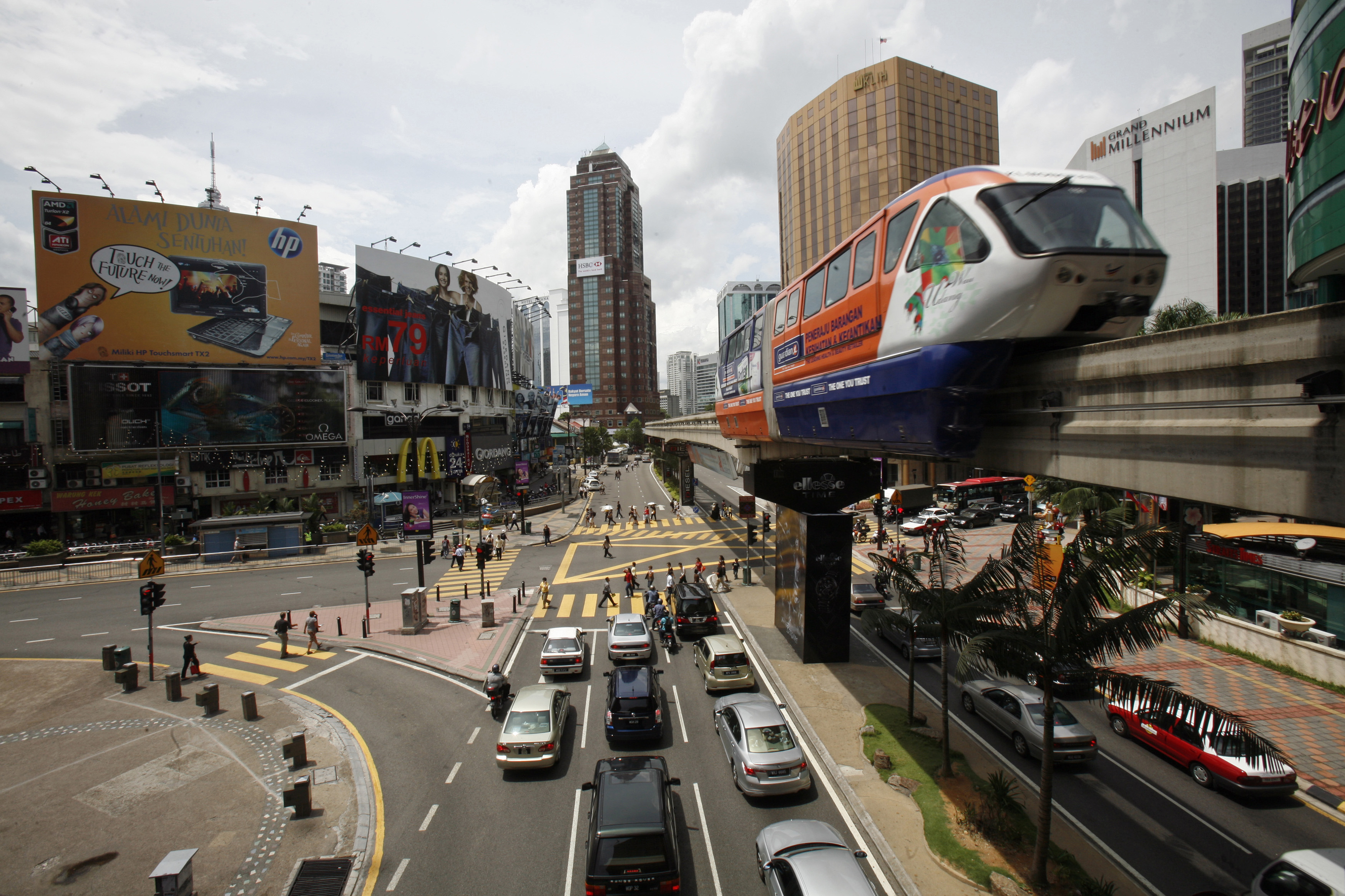 A train moves along a raised railway track, with several lanes of cars underneath in what looks like a busy city centre