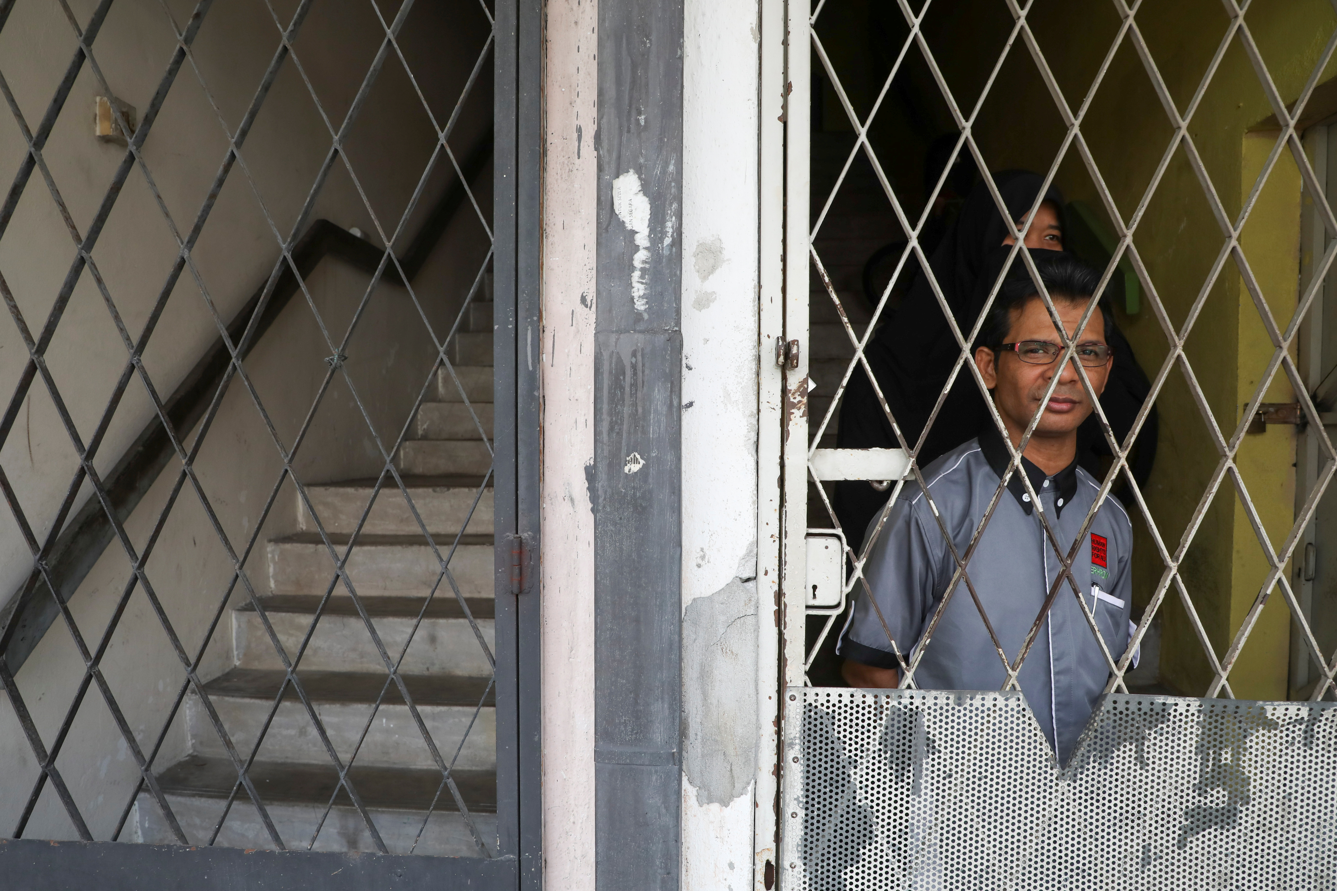 Rohingya refugee and activist Zafar Ahmad Abdul Ghani and his wife look out from behind a metal grille at their home in Kuala Lumpur, Malaysia.