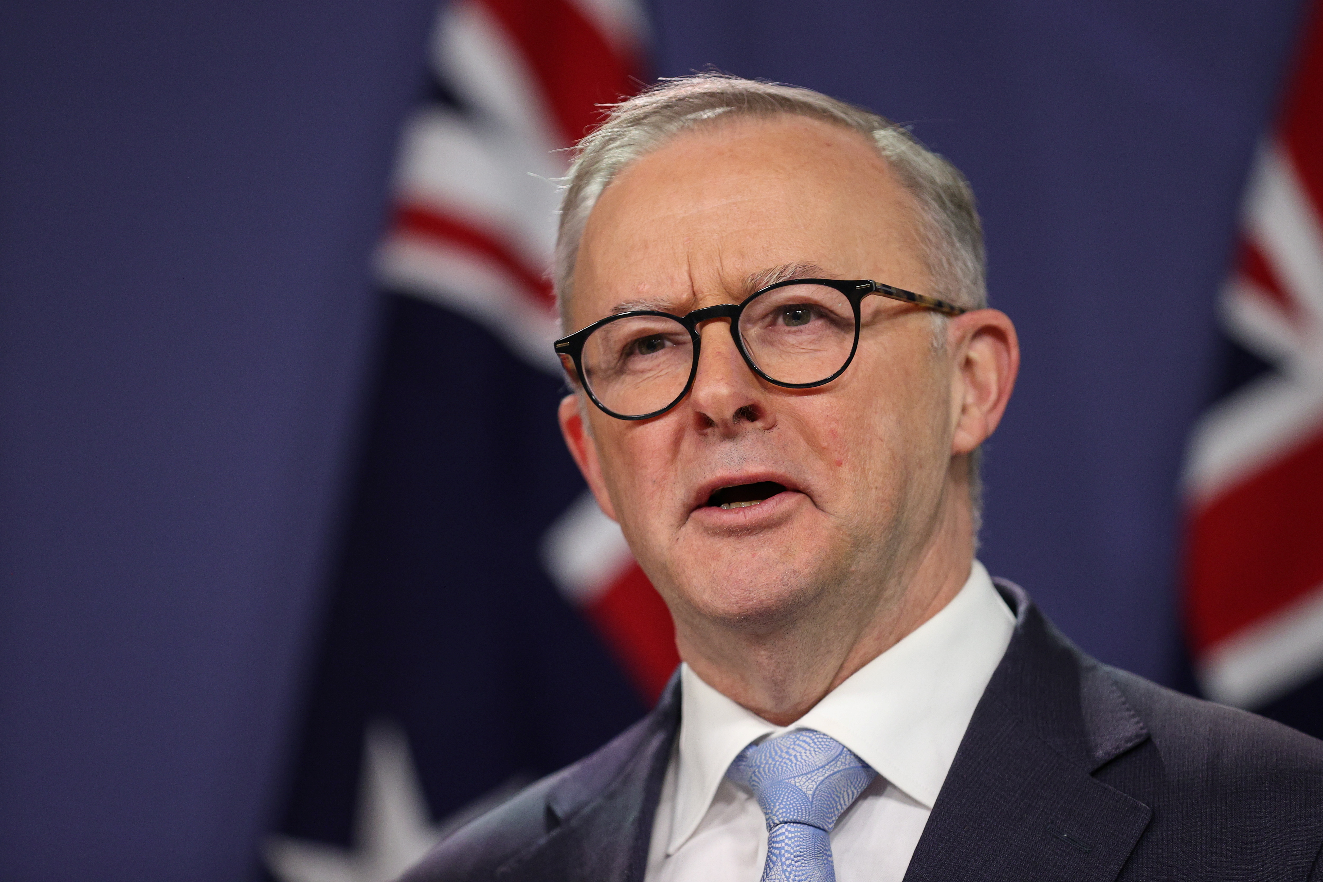 Australian Prime Minister Anthony Albanese against blue background and two Australian flags