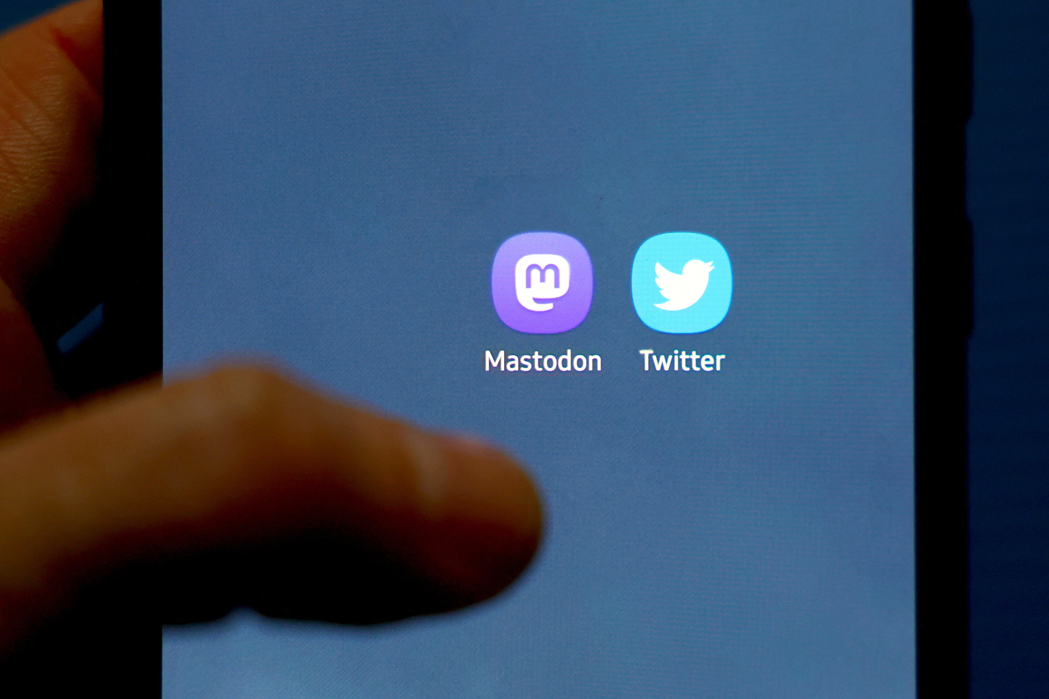 A person holds a mobile phone showing the Mastodon and Twitter icon.