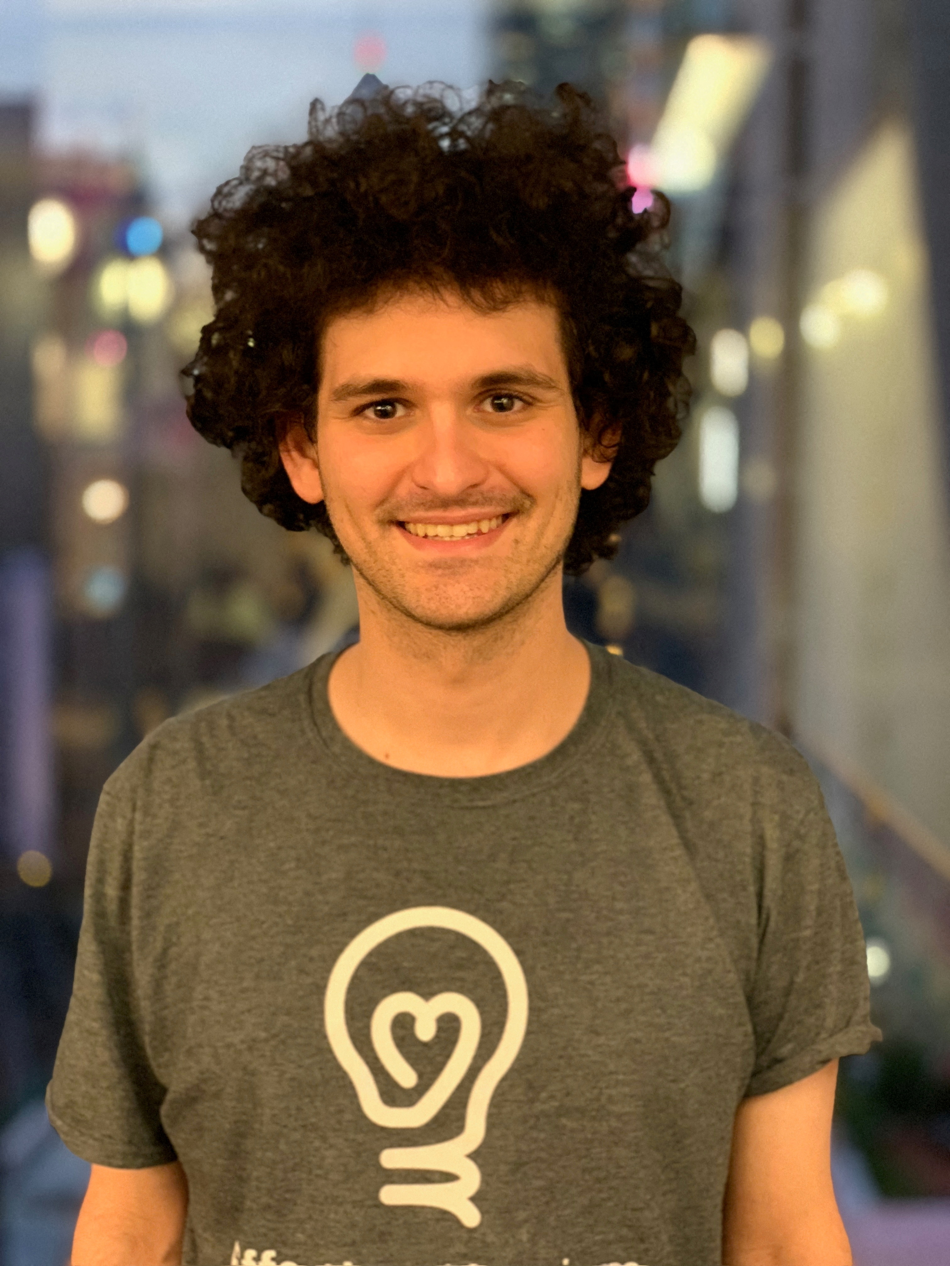 Sam Bankman-Fried, smiling, in a grey t-shirt with a stylised light bulb on it