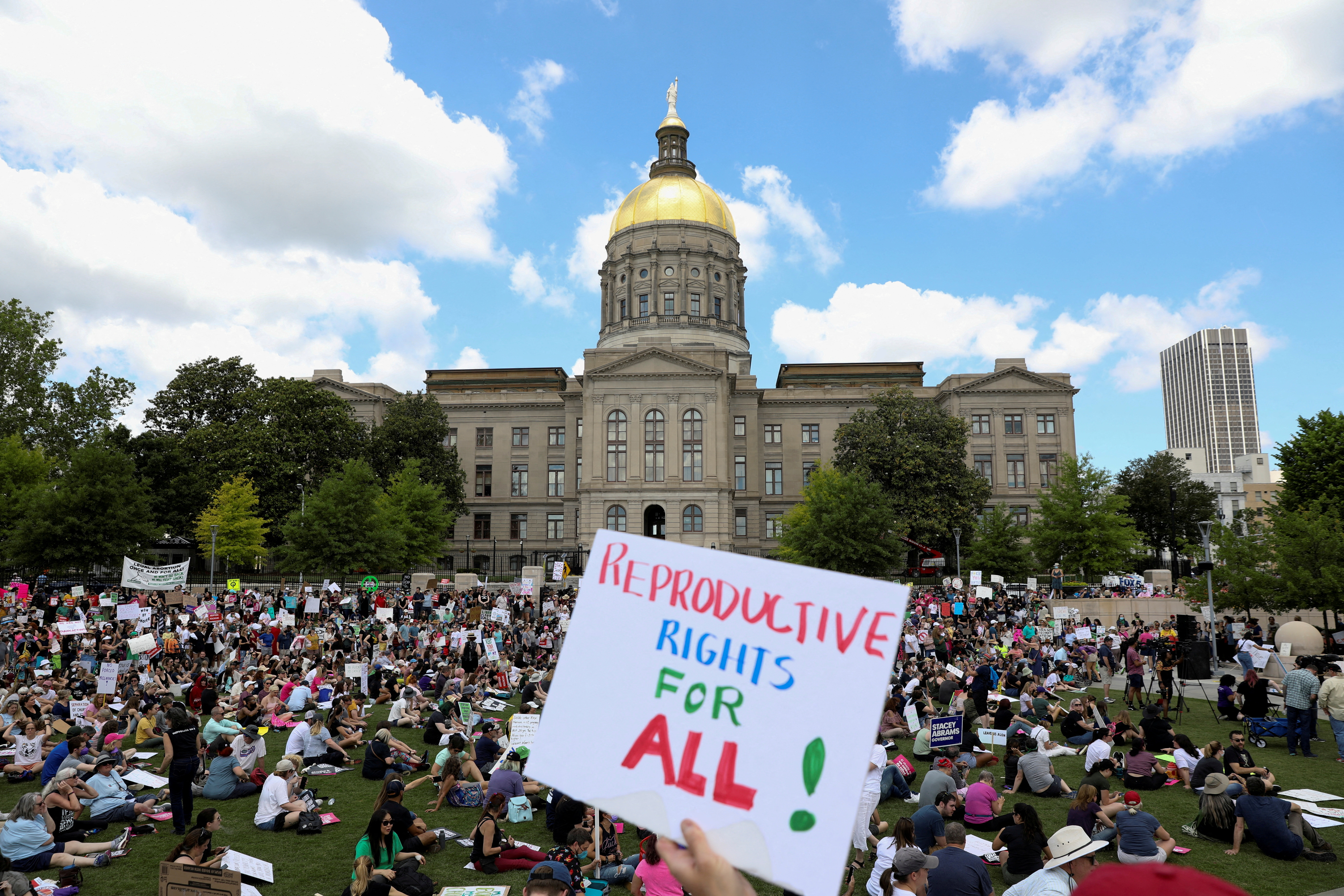 Hundreds of activists sit on the lawn in front of the building while one poster is seen close-up saying: 'Reproductive rights for ALL'