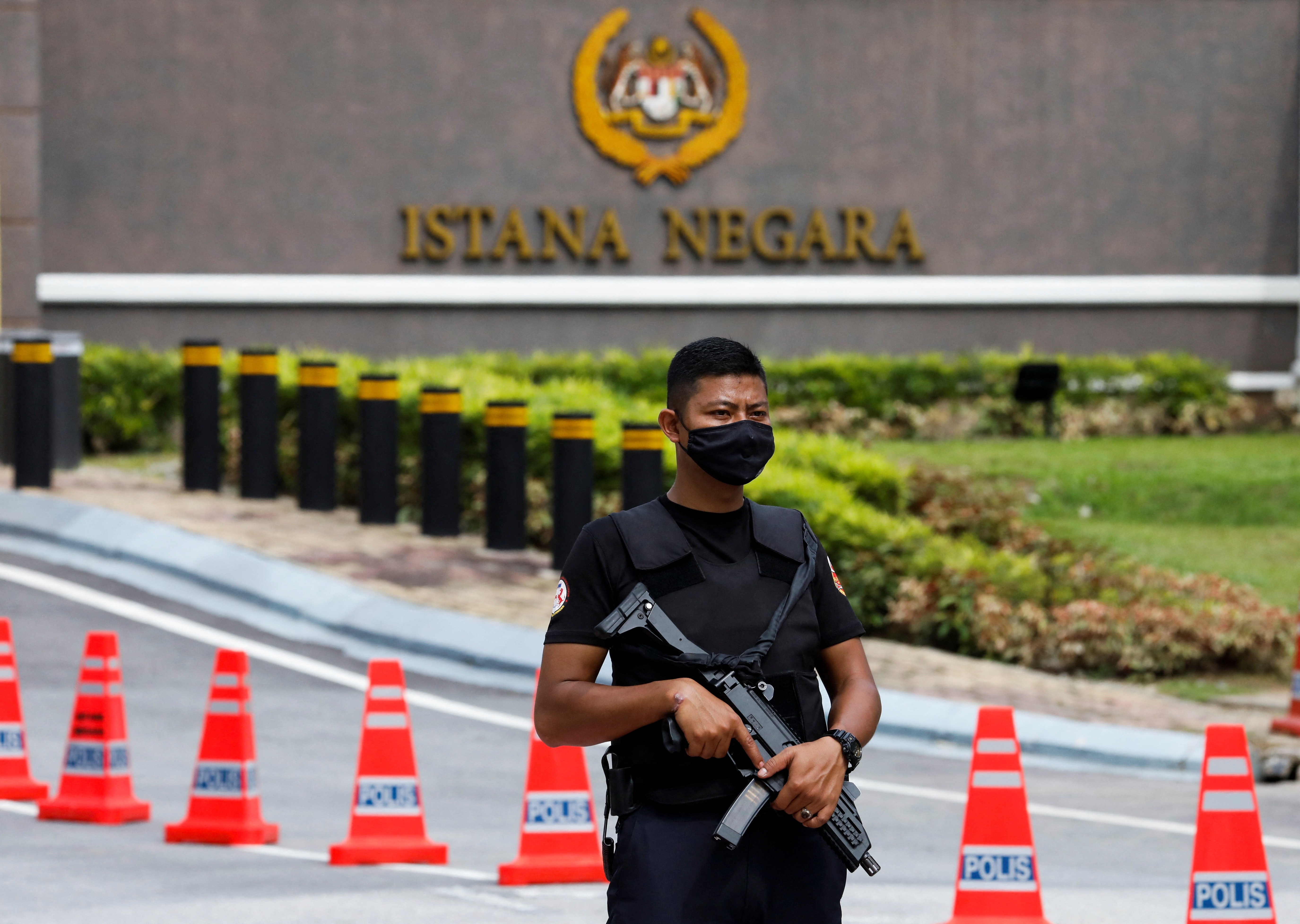 An armed Malaysian policeman in black uniform and facemask outside the king's palace