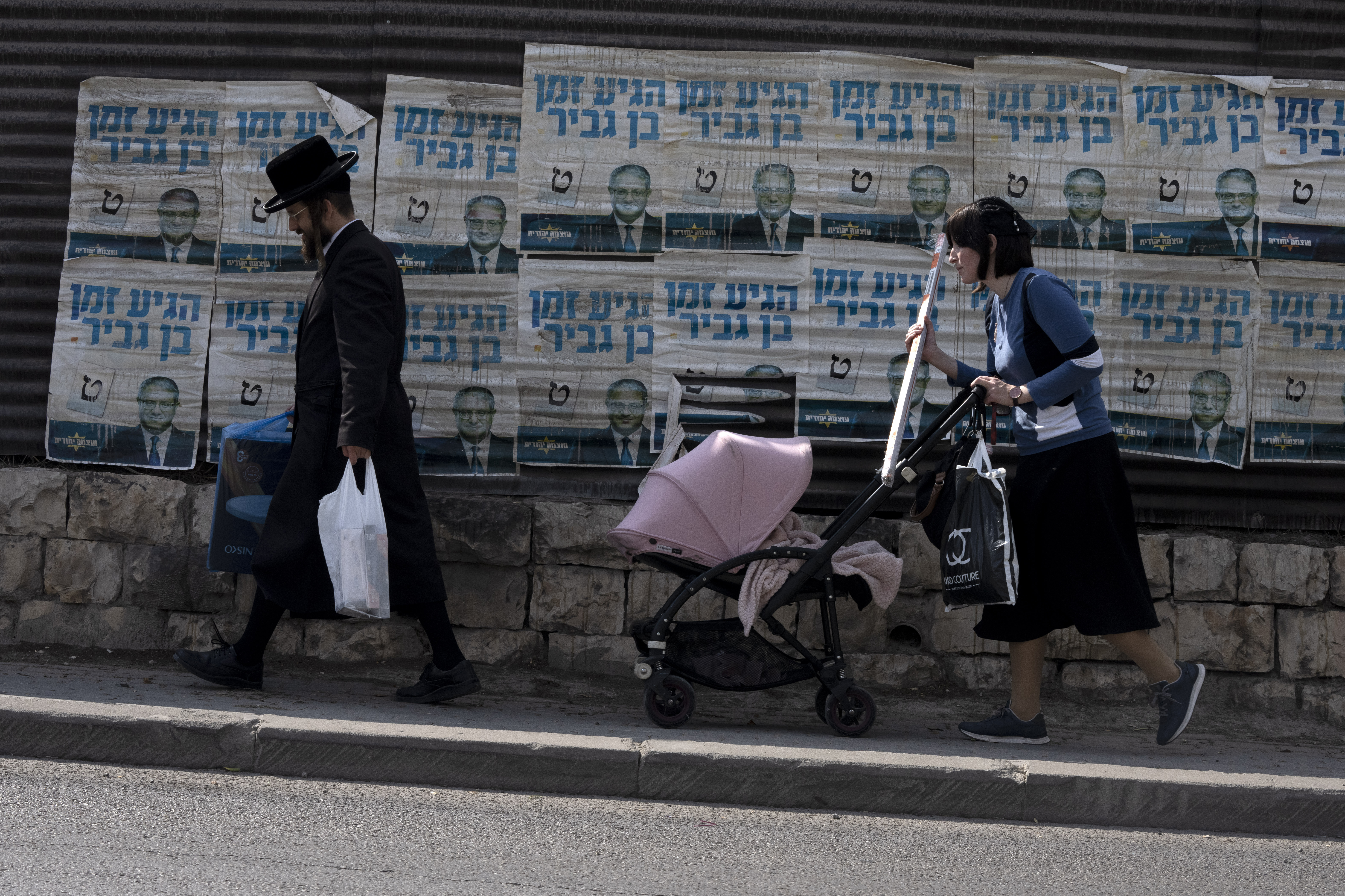 An ultra-Orthodox Jewish couple with a baby in a pushchair walk past election campaign posters for Israeli legislator Itamar Ben Gvir.