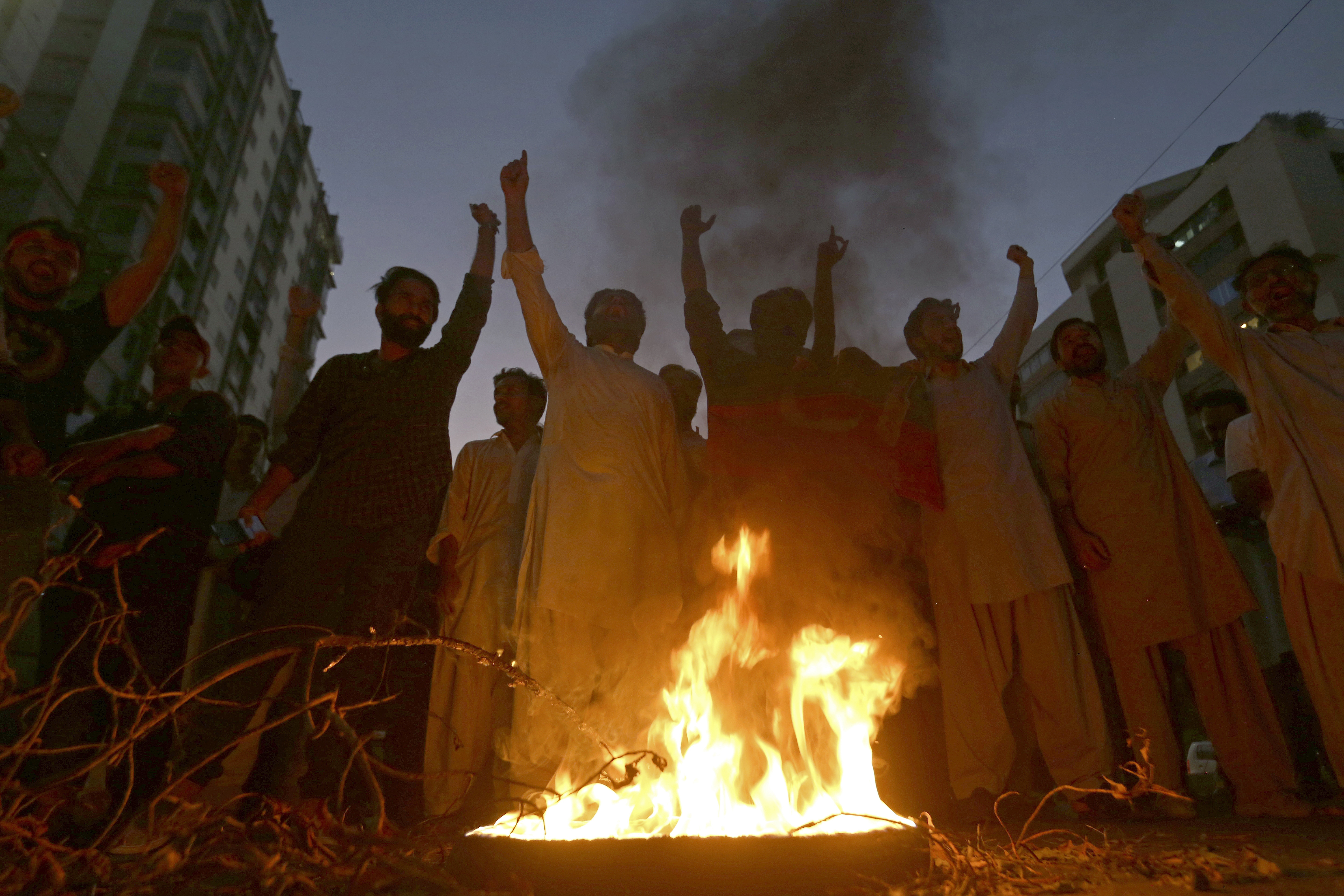 Supporters of former Pakistani Prime Minister Imran Khan's party, Pakistan Tehreek-e-Insaf, chant slogans next to a burning tire during a protest to condemn a shooting incident on their leader's convoy, in Karachi, Pakistan, Thursday, Nov. 3, 2022. A gunman opened fire Thursday at a campaign truck carrying Khan, wounding him slightly in the leg and killing one of his supporters, his party and police said. Nine others were also wounded. (AP Photo/Fareed Khan)