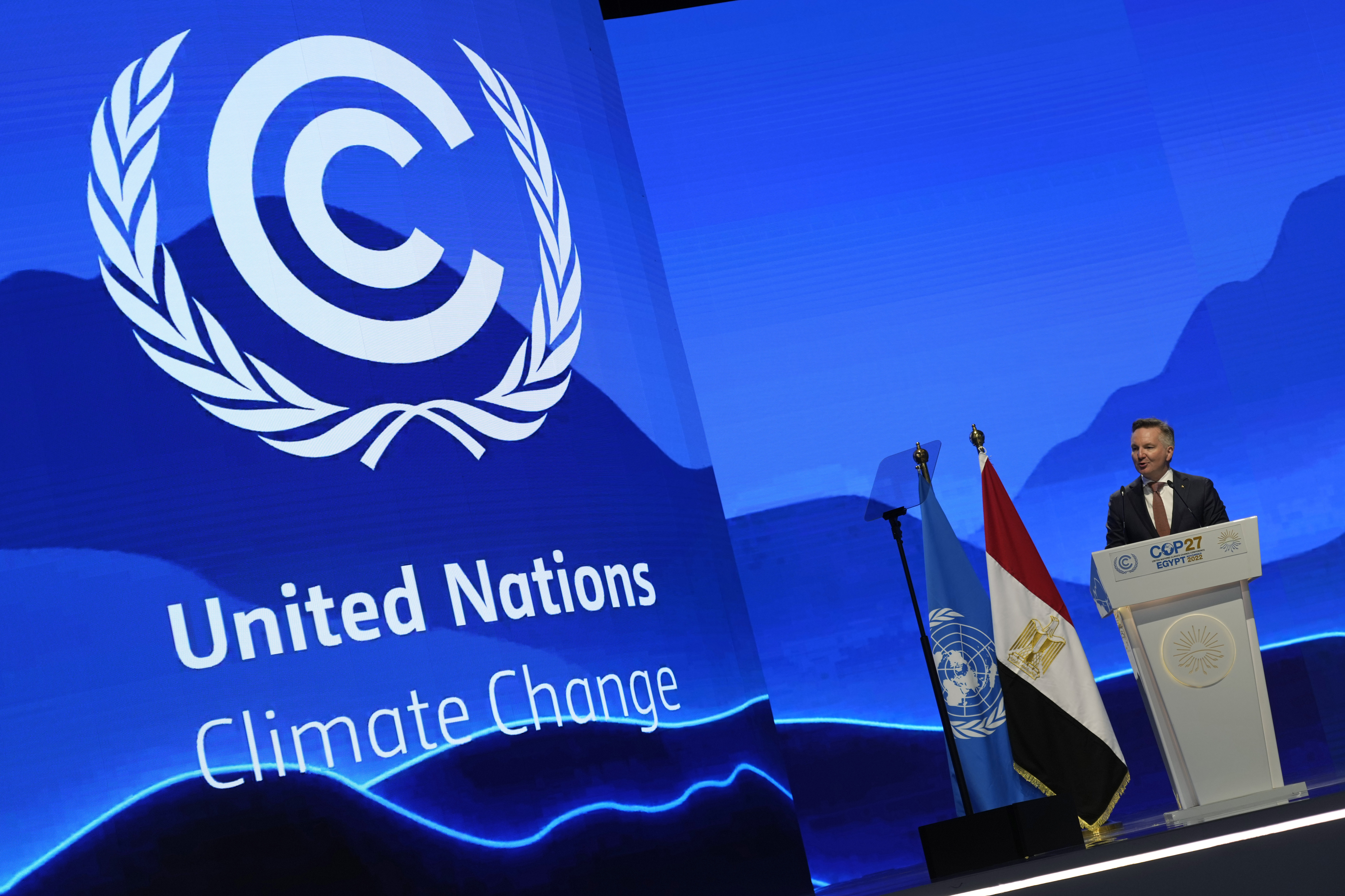 Australia's climate minister Christopher Bowen making a speech at COP27 against a bright blue backdrop showing the UN climate talks logo