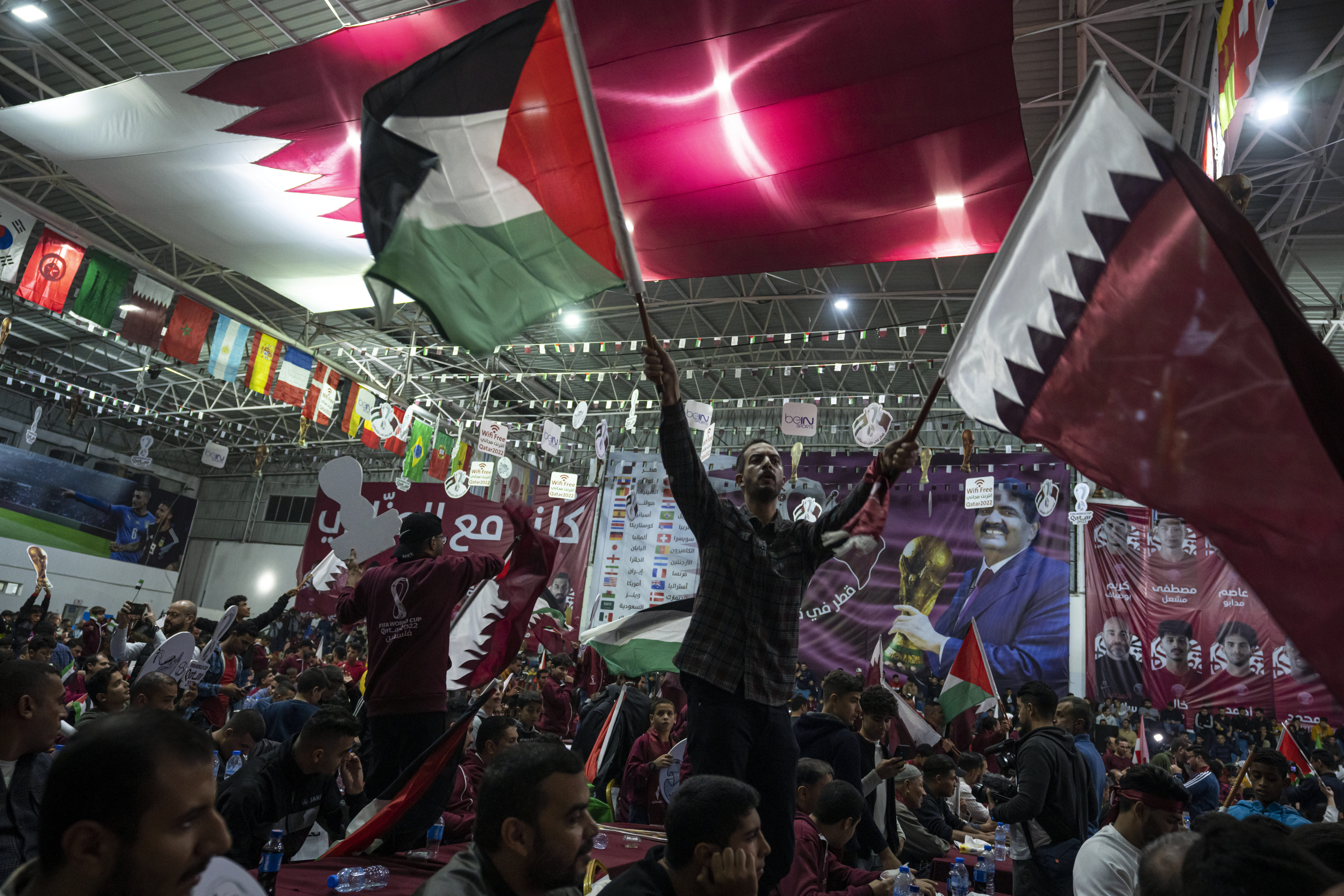 Palestinian football fans waving Qatari and Palestinian flags watch a live broadcast of 2022 World Cup opening match in occupied Gaza.