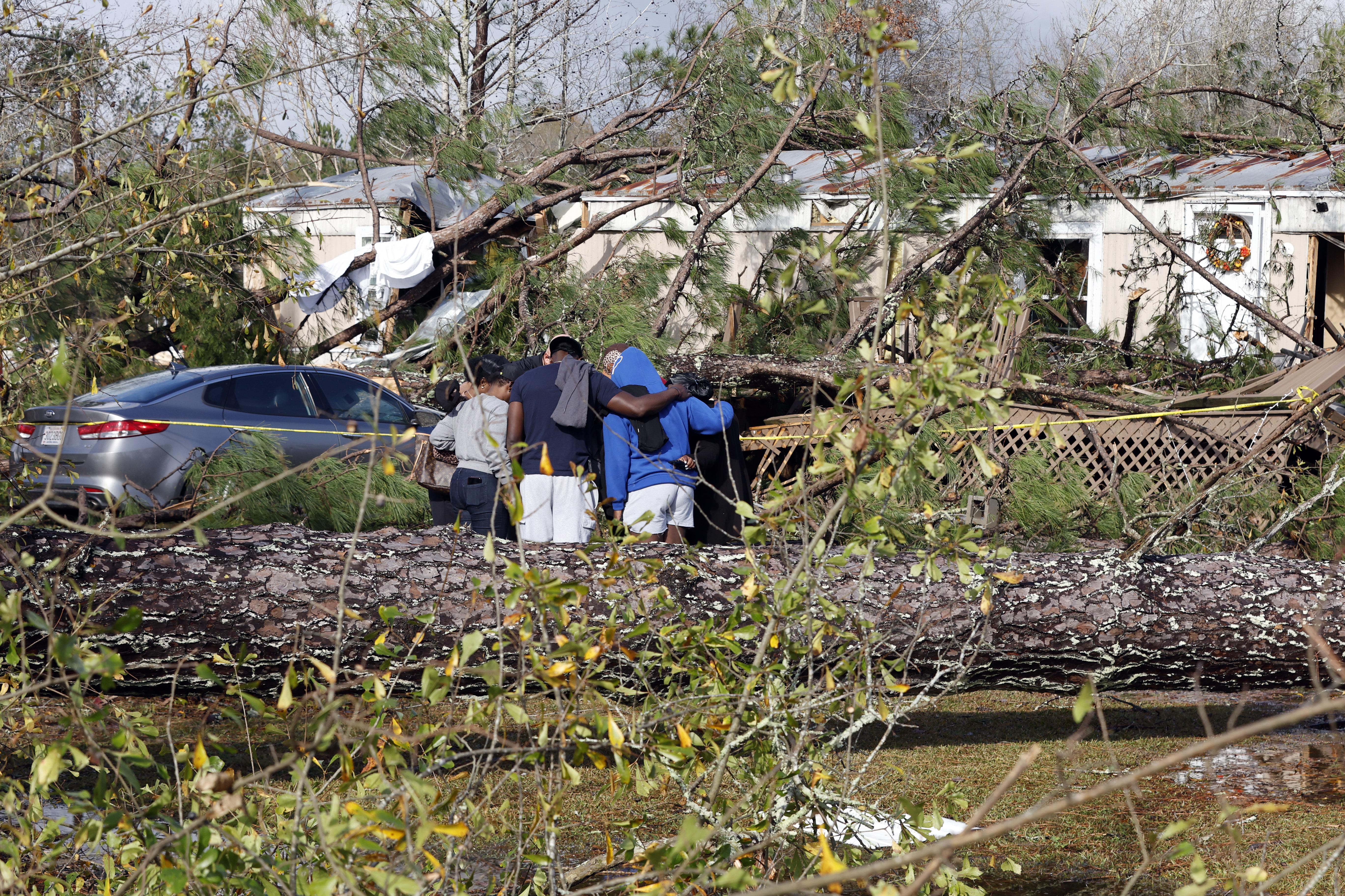 Friends and family pray outside a damaged mobile home,