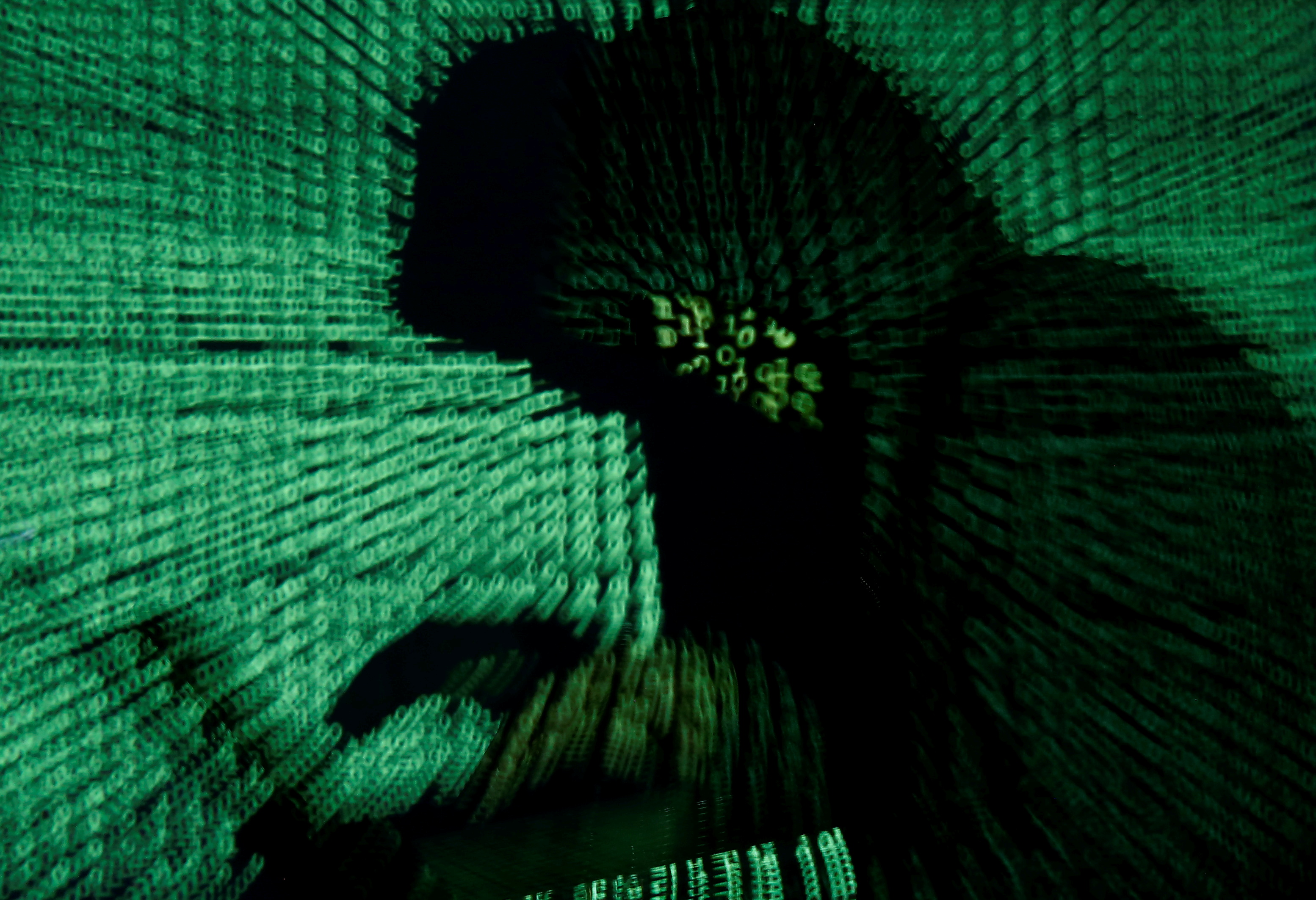 A stylised photo showing a fuzzy silhouette of a person at a laptop with green code projected over them.