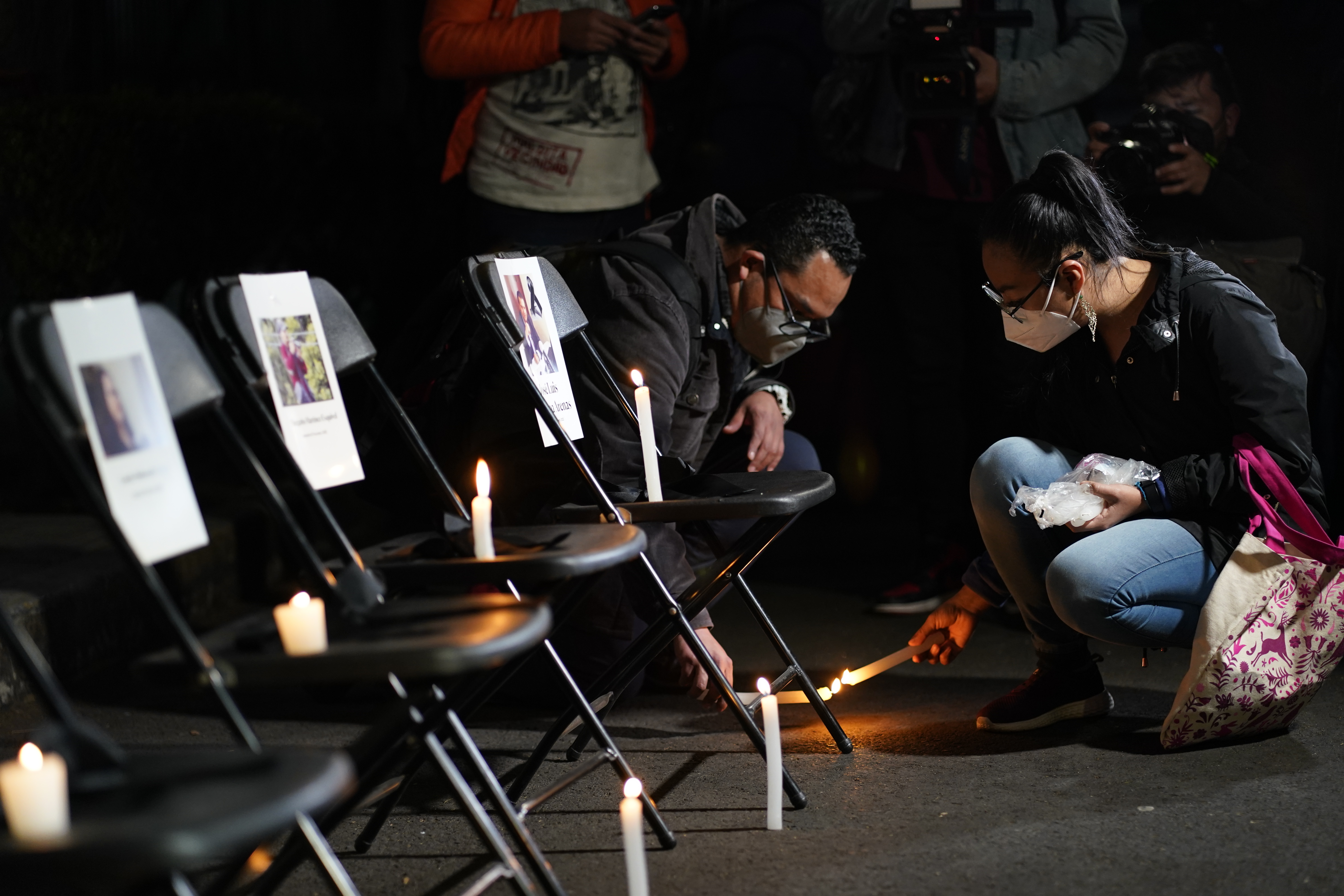 A couple lights a candle next to a vigil for slain journalists, with pictures taped to empty chairs
