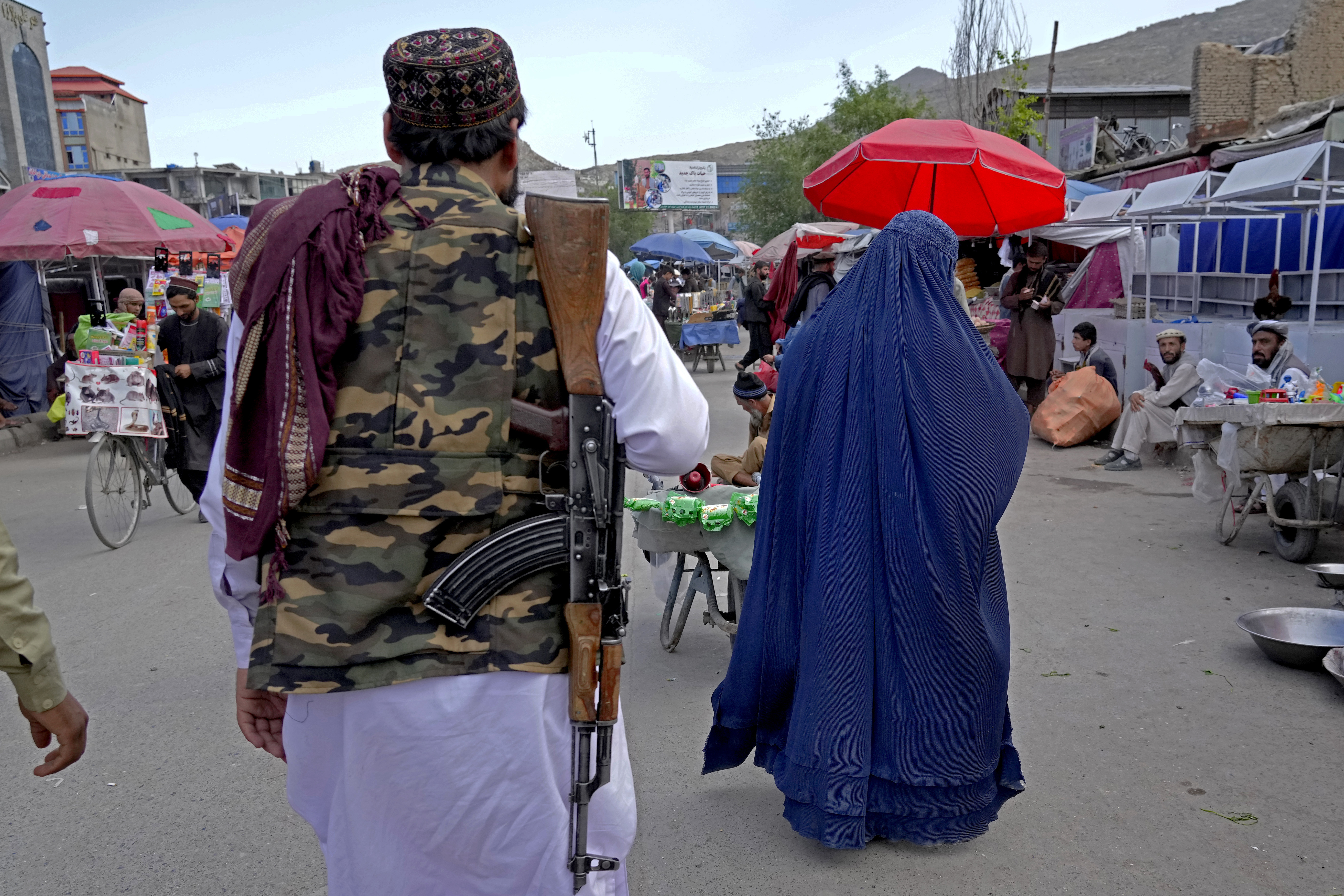 A woman wearing a burka walks through the old market as a Taliban fighter stands guard, in downtown Kabul