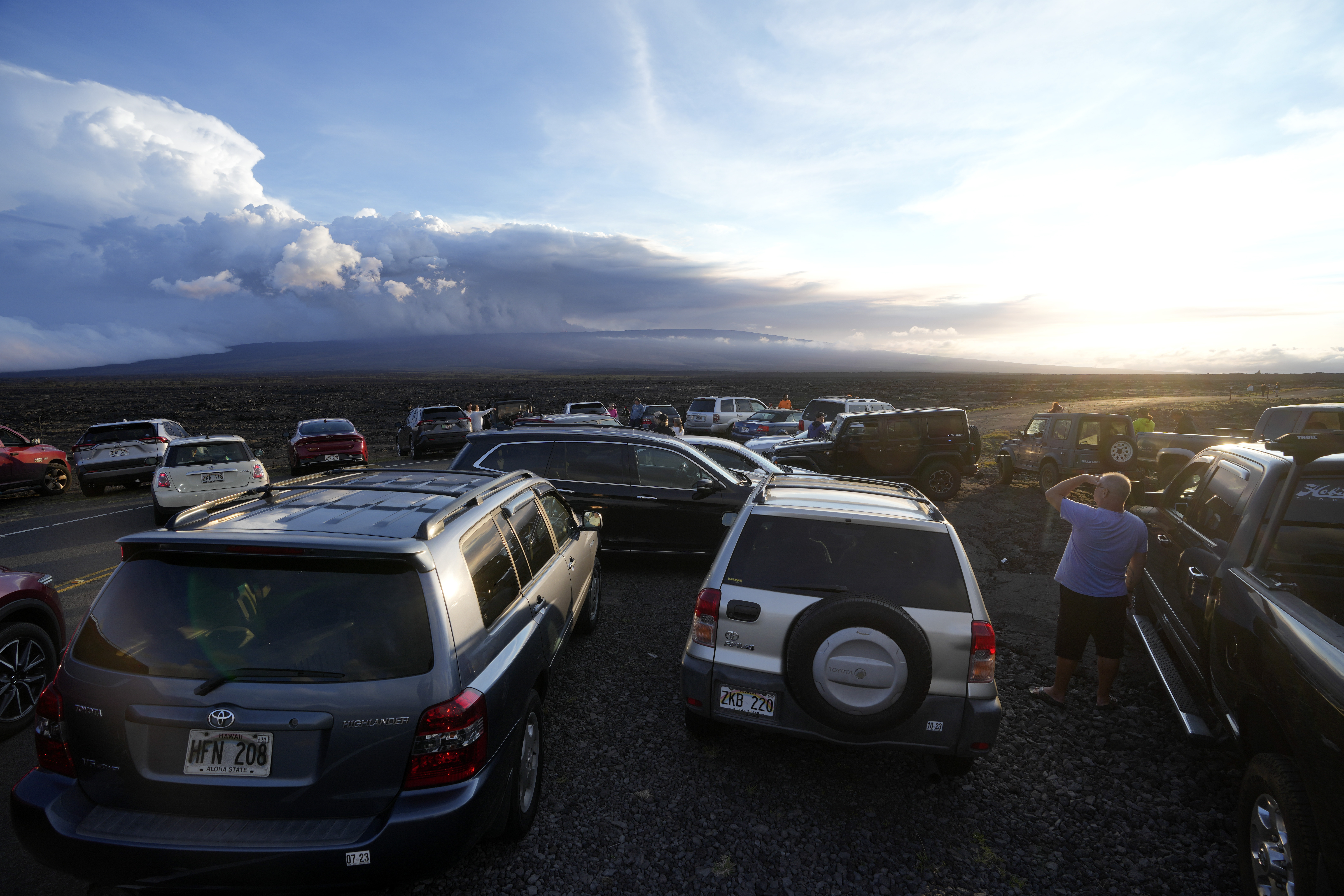 An overflow of cars sit in a parking lot near the Mauna Loa volcano