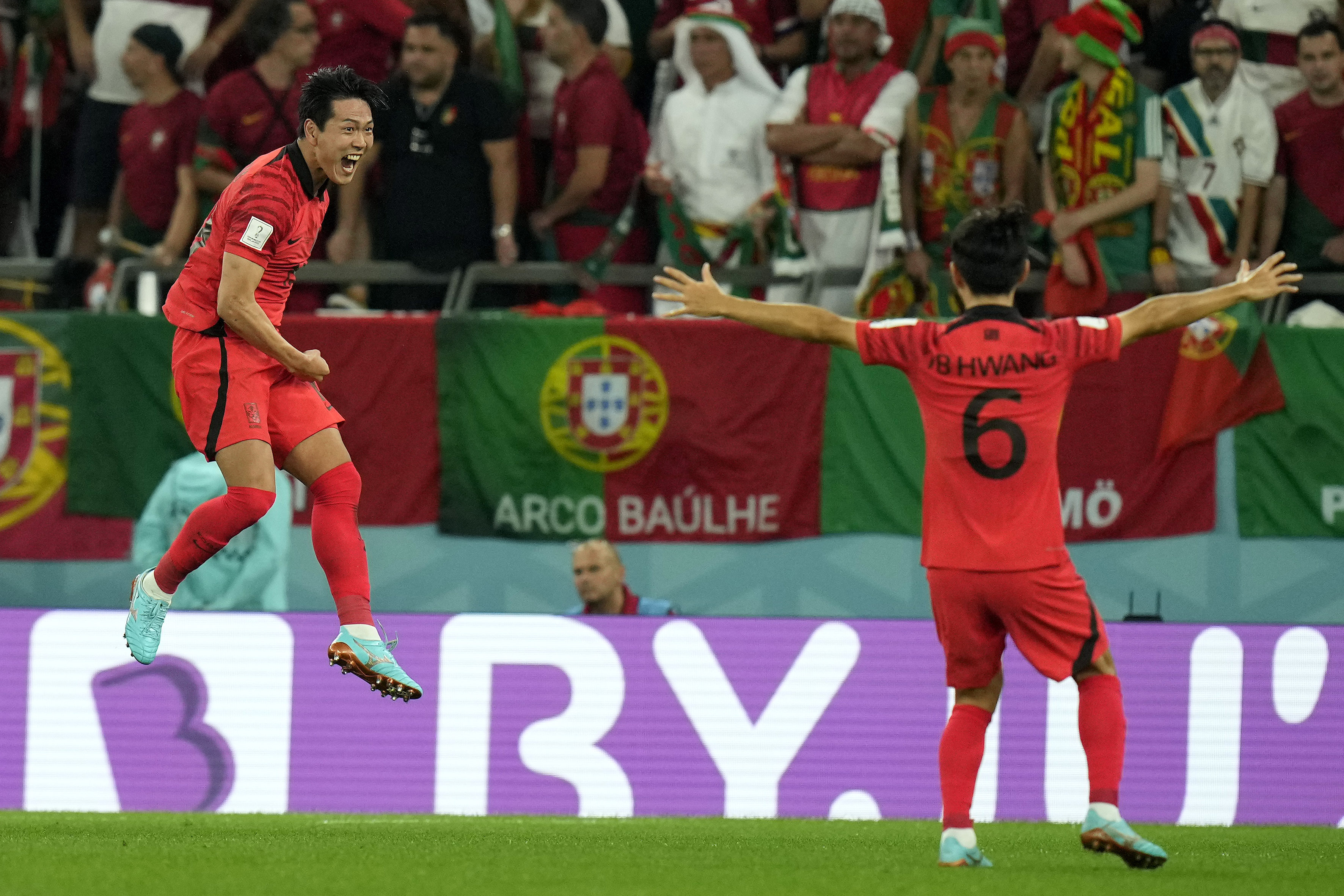 Na Sangho in mid-air smiles excitedly at Hwang Inbeom who has his arms out and is facing the crowd in the stands