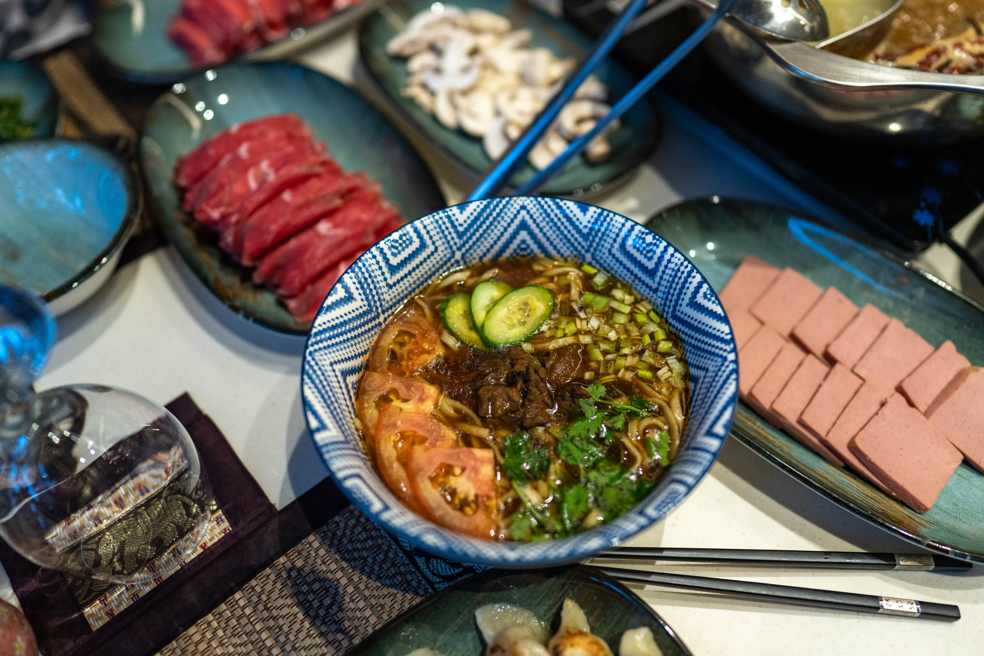 Overhead shot of a bowl of noodle soup topped with veggies and herbs and stir-fried beef