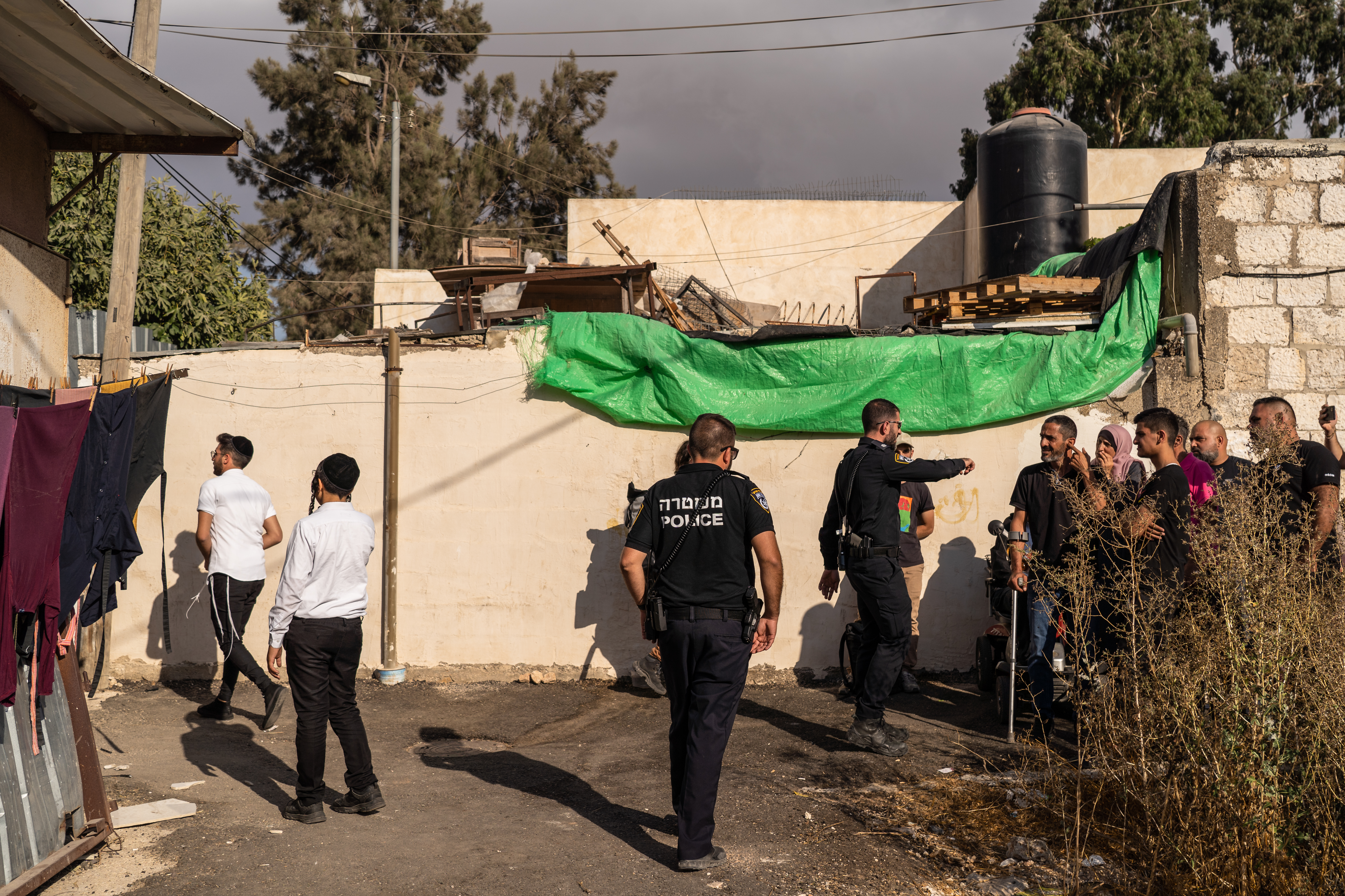 Israeli security force gesture at Palestinians while Jewish settlers stand on the left of the picture