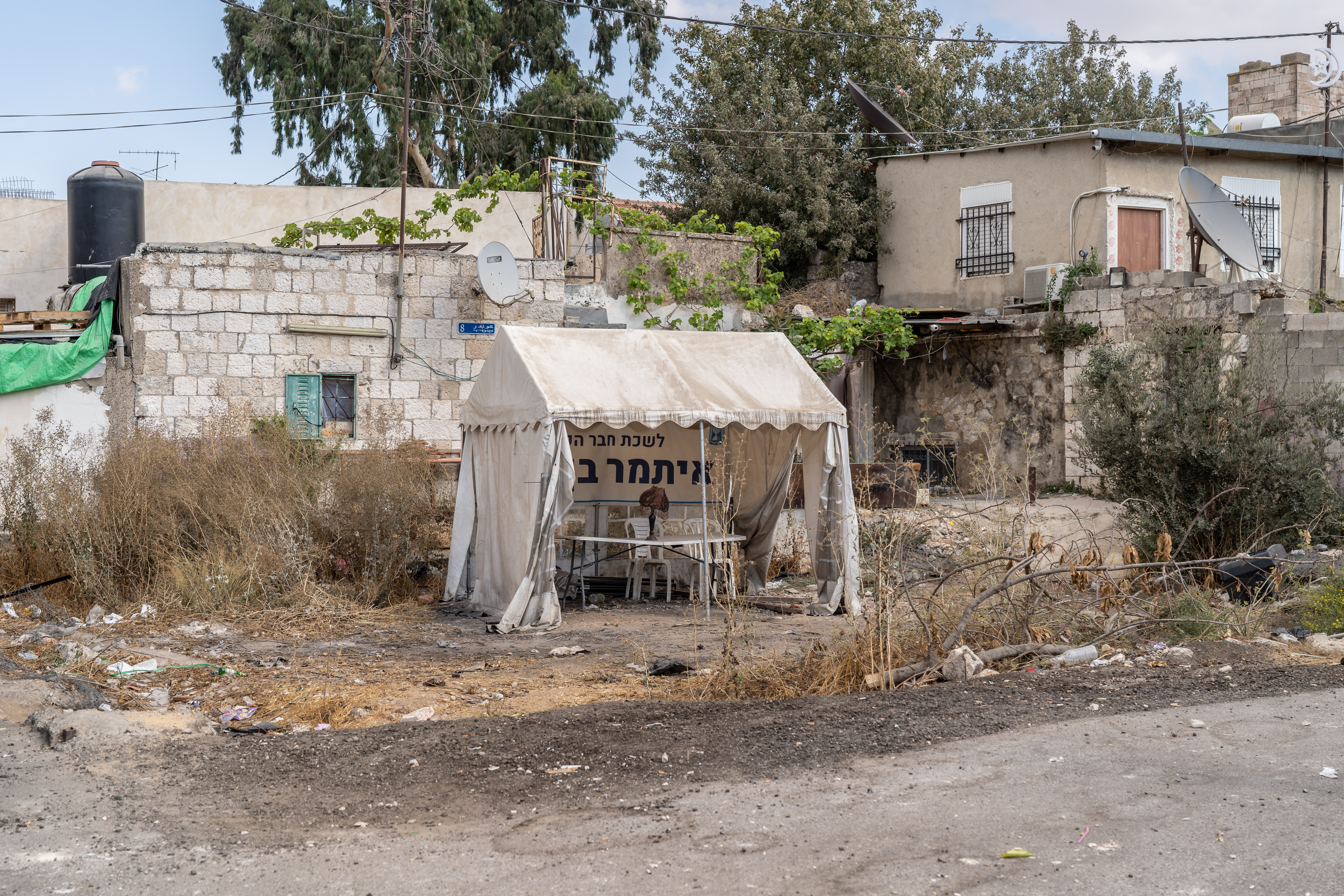 A tent stands in the middle of an empty plot of land with houses in the background