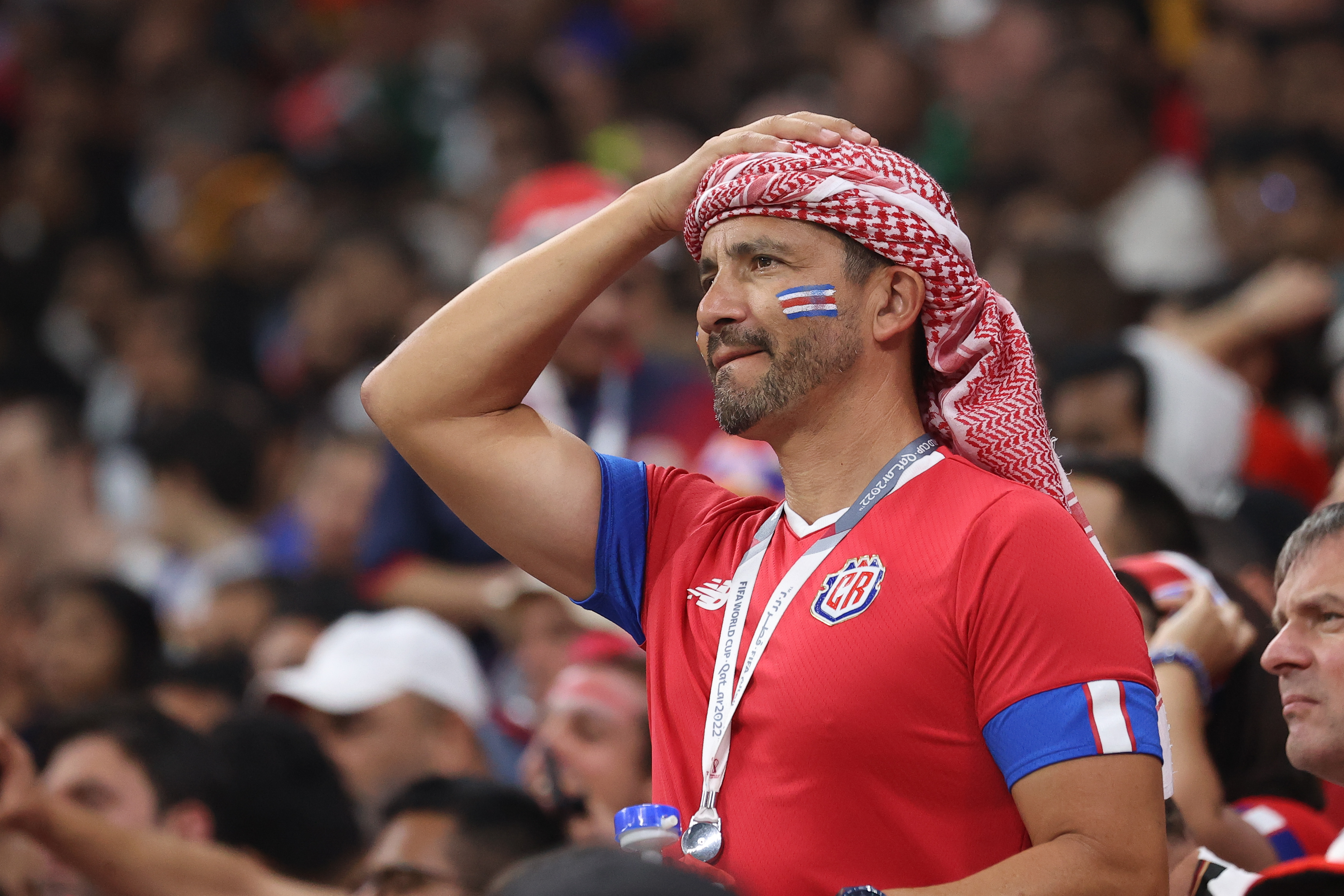 Costa Rica fan wearing red and blue holds his head in disappointment. The Costa Rica flag is painted on his cheek.