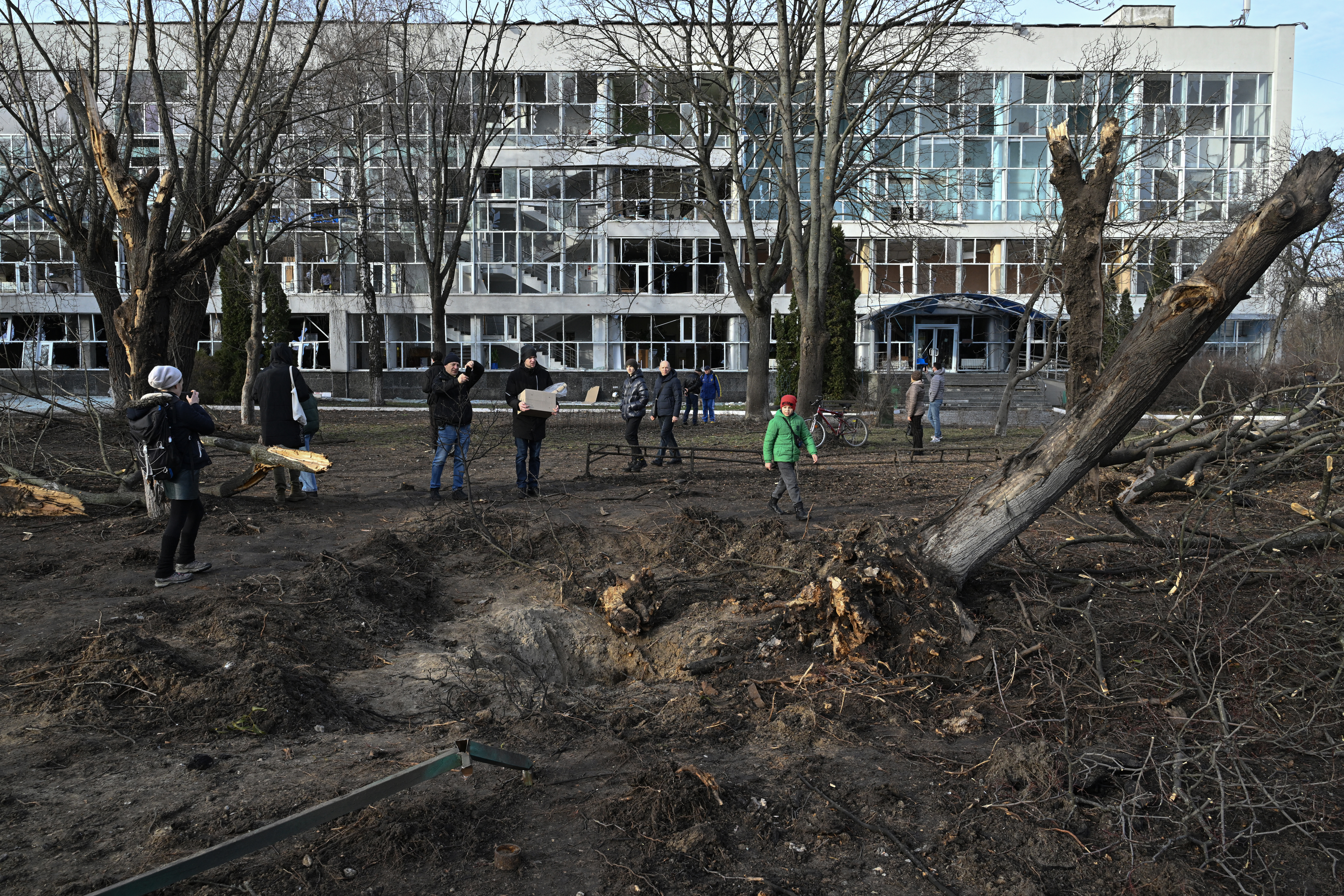 Bystanders look at a crater next to an educational building in Kyiv on January 1, 2023, which was damaged by a missile strike on the previous day, amid the Russian invasion of Ukraine.