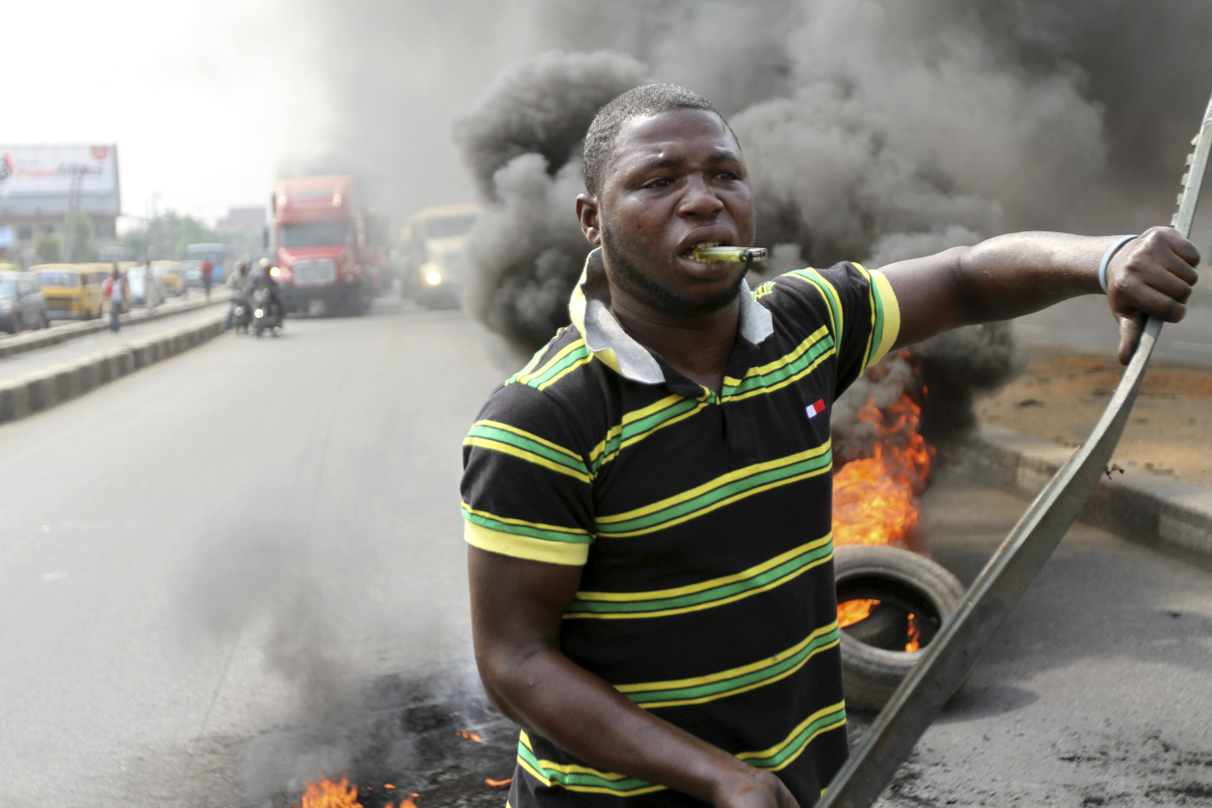 A protester walks past burning tyres while biting a lighter during a rally against fuel subsidy removal on Ikorodu road in Nigeria's commercial capital Lagos January 3, 2012. Hundreds of demonstrators in Nigeria's commercial capital Lagos shut petrol stations, formed human barriers along motorways and hijacked buses on Tuesday in protest against the shock doubling of fuel prices after a government subsidy was removed. REUTERS/Akintunde Akinleye (NIGERIA - Tags: CIVIL UNREST POLITICS ENERGY)