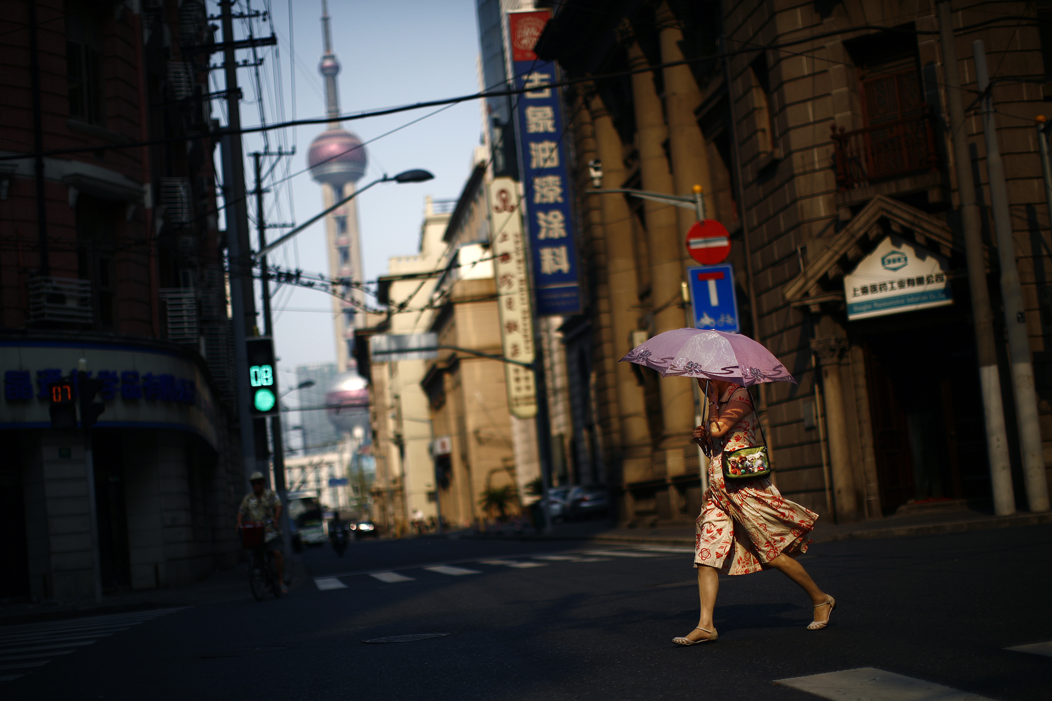 A woman walks across a Shanghai street with an umbrella to protect herself from the sun.