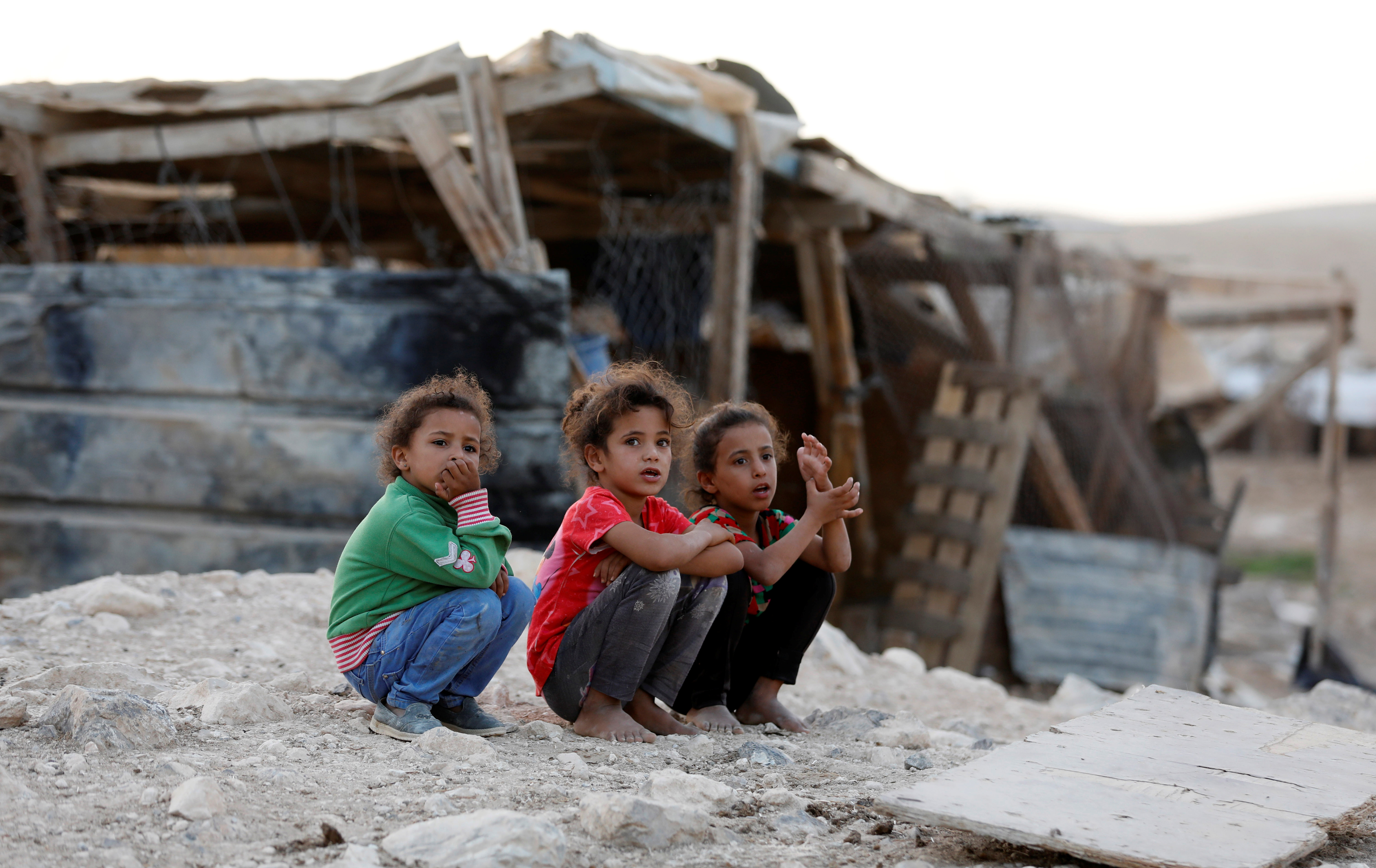 Three girls squat in front of a shack