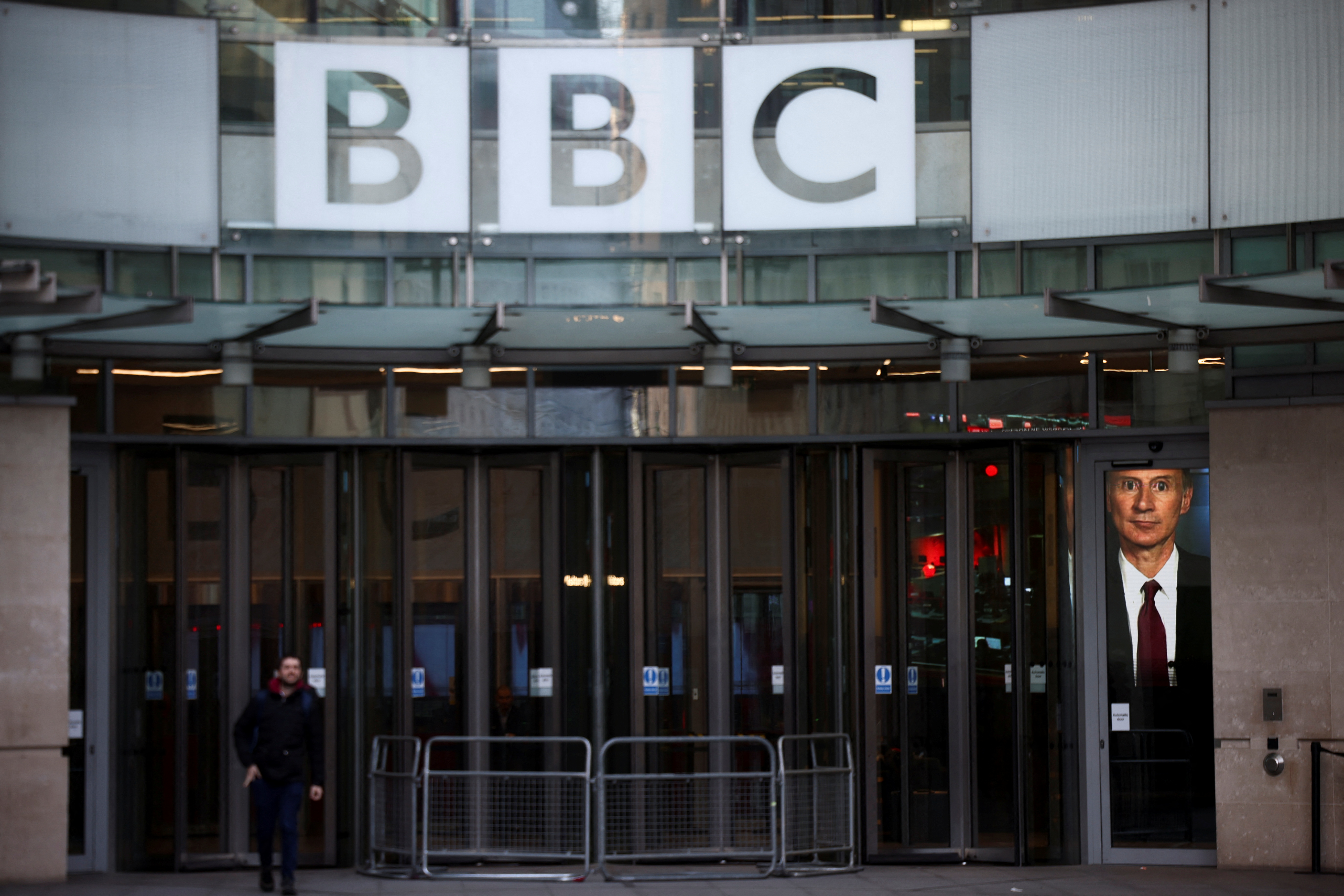 A man outside walks past the entrance to the BBC as a screen shows an interview with British Chancellor of the Exchequer Jeremy Hunt in the foyer in London, the United Kingdom in October 2022..