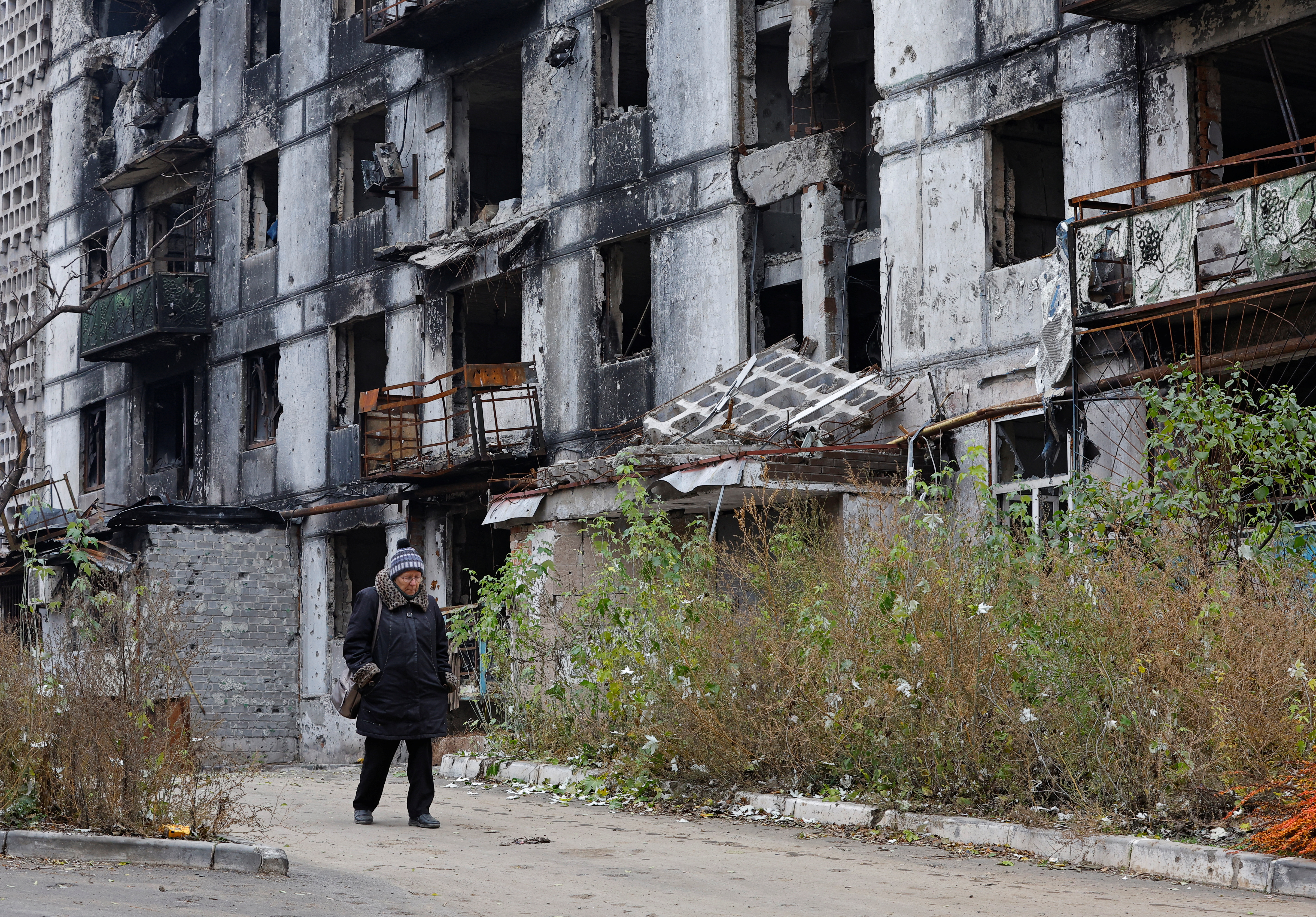 A woman walks past a damaged building in Mariupol