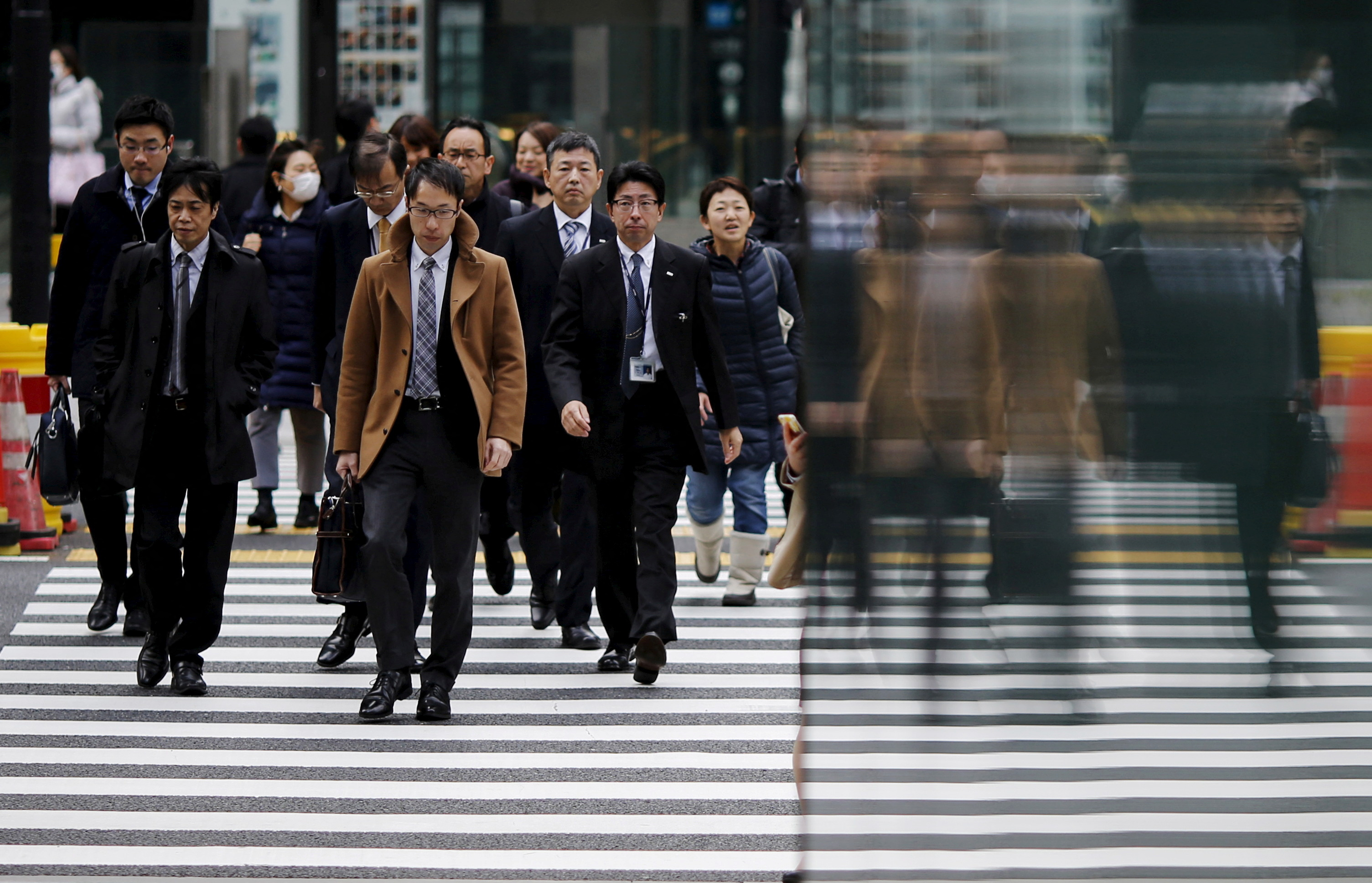 People crossing the road in Tokyo, Japan. Most are men in suits but there are a few women.