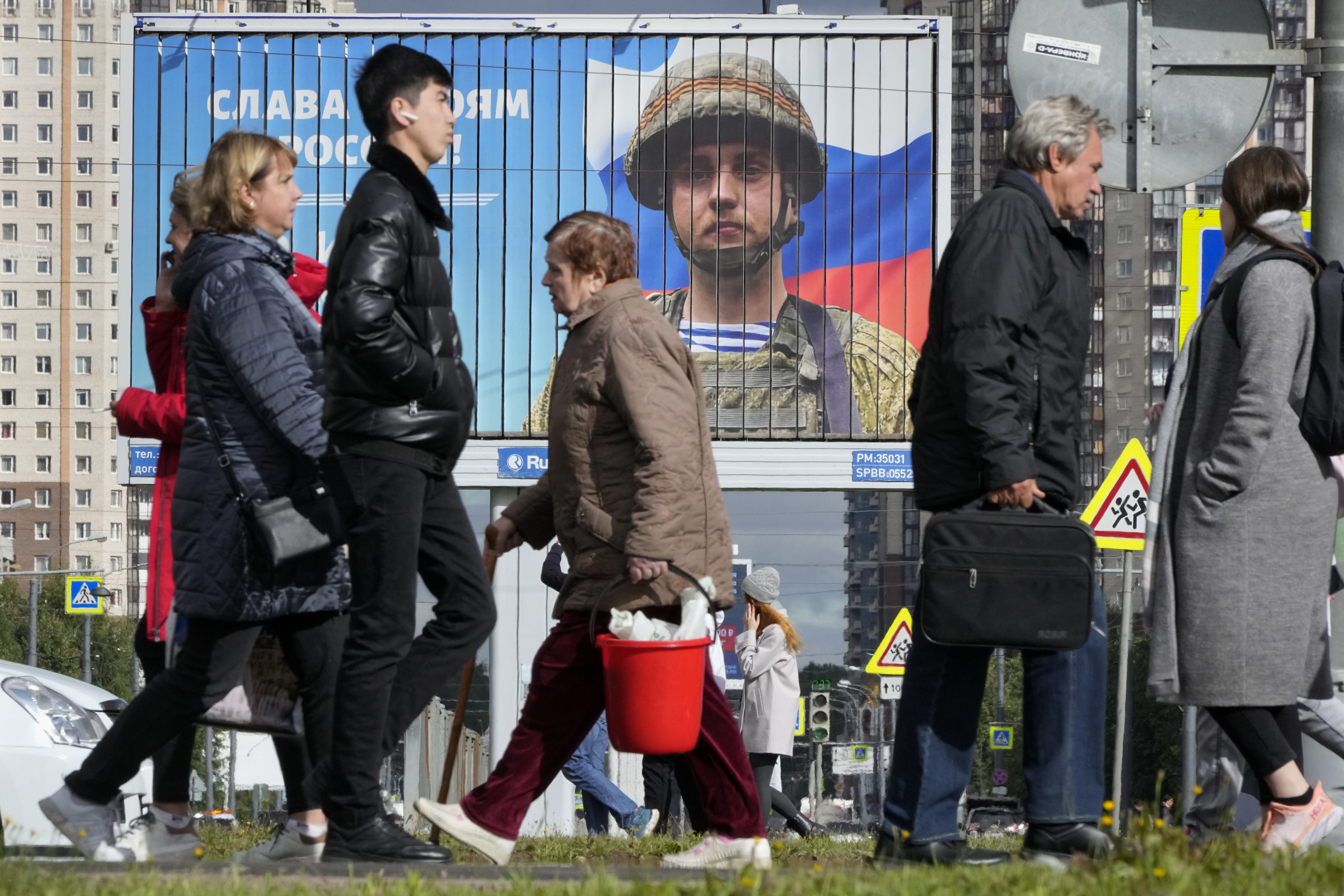People in St Petersburg walk past a billboard with a portrait of a Russian soldier awarded for action in Ukraine