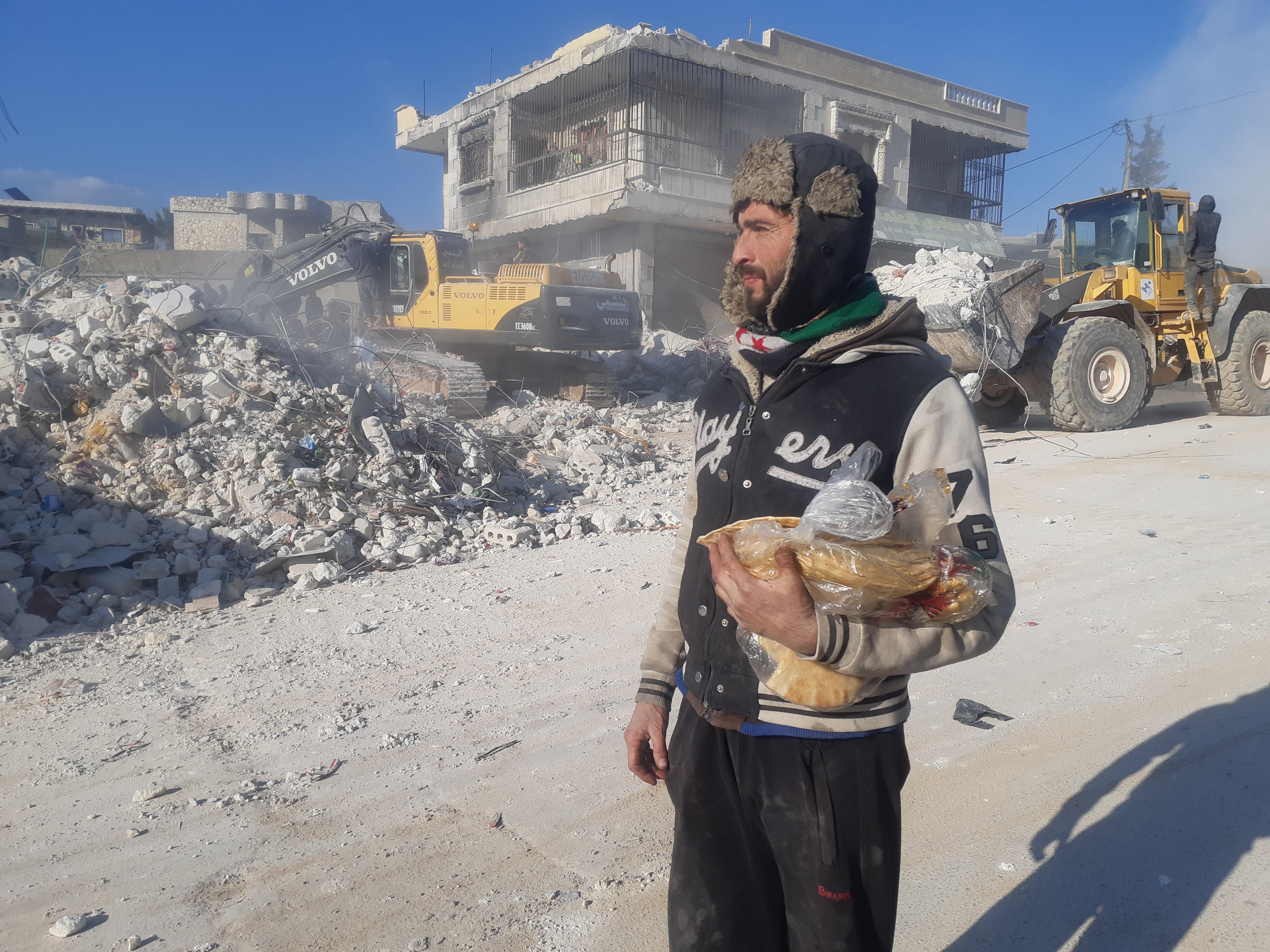 Man carrying a bag of bread through a destroyed town
