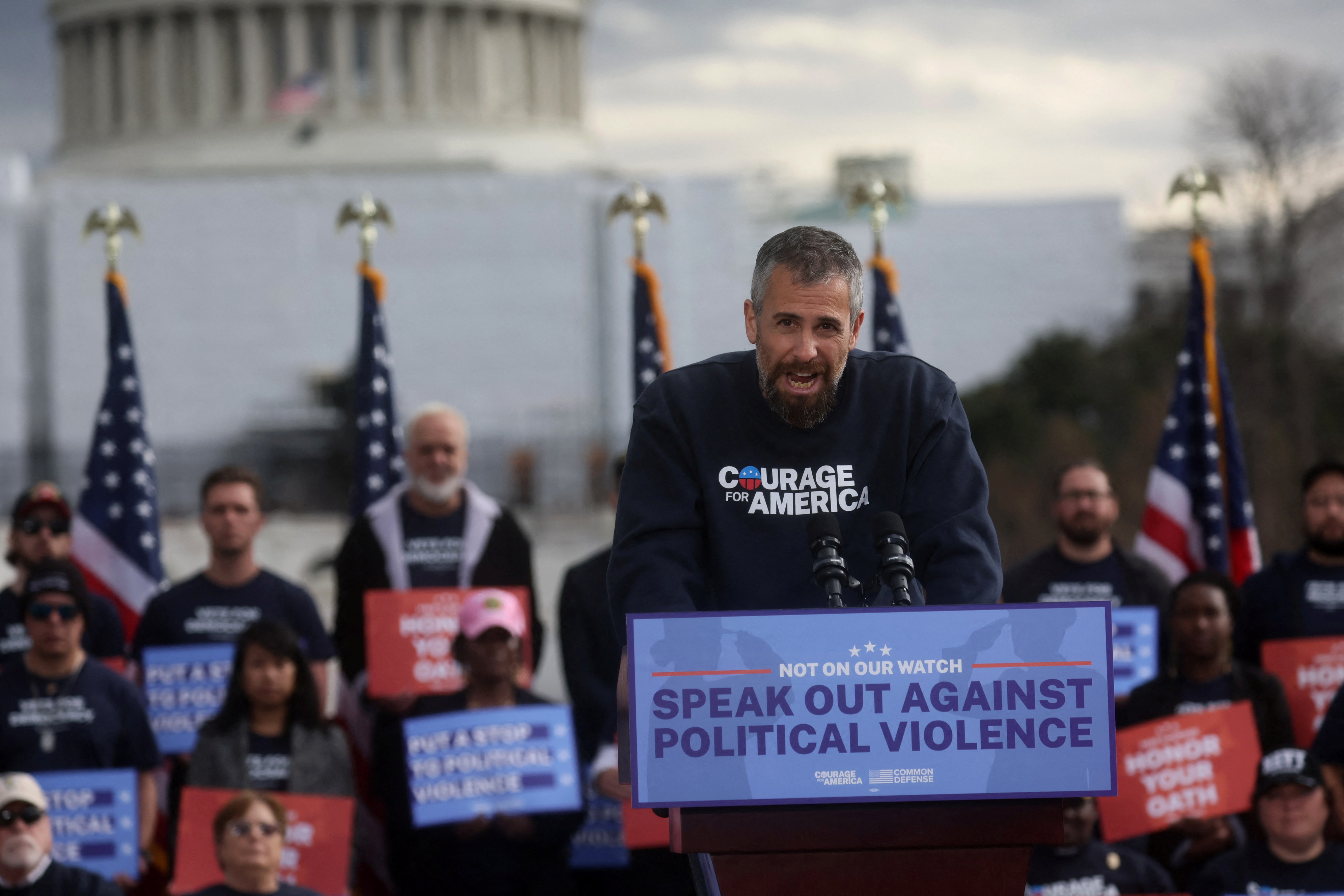 Michael Fanone speaks at a rally in front of the Capitol against political violence. The pulpit he is standing at says 'speak out against political violence' on it