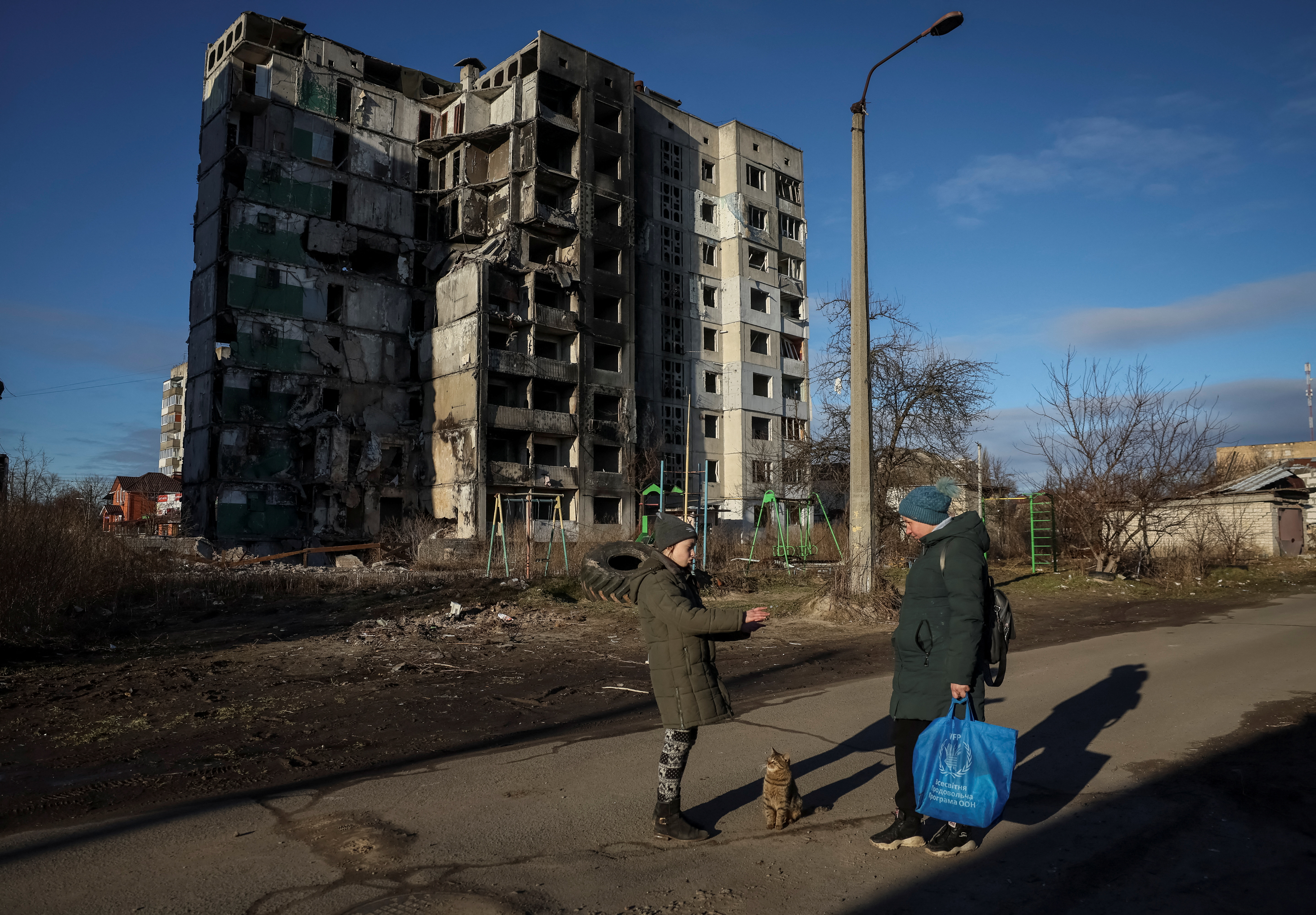 Veronika Krasevych, an 11-year-old Ukrainian girl feeds a feral cat as her mother Oksana stands nearby near their building destroyed by Russian military strike in the town of Borodianka