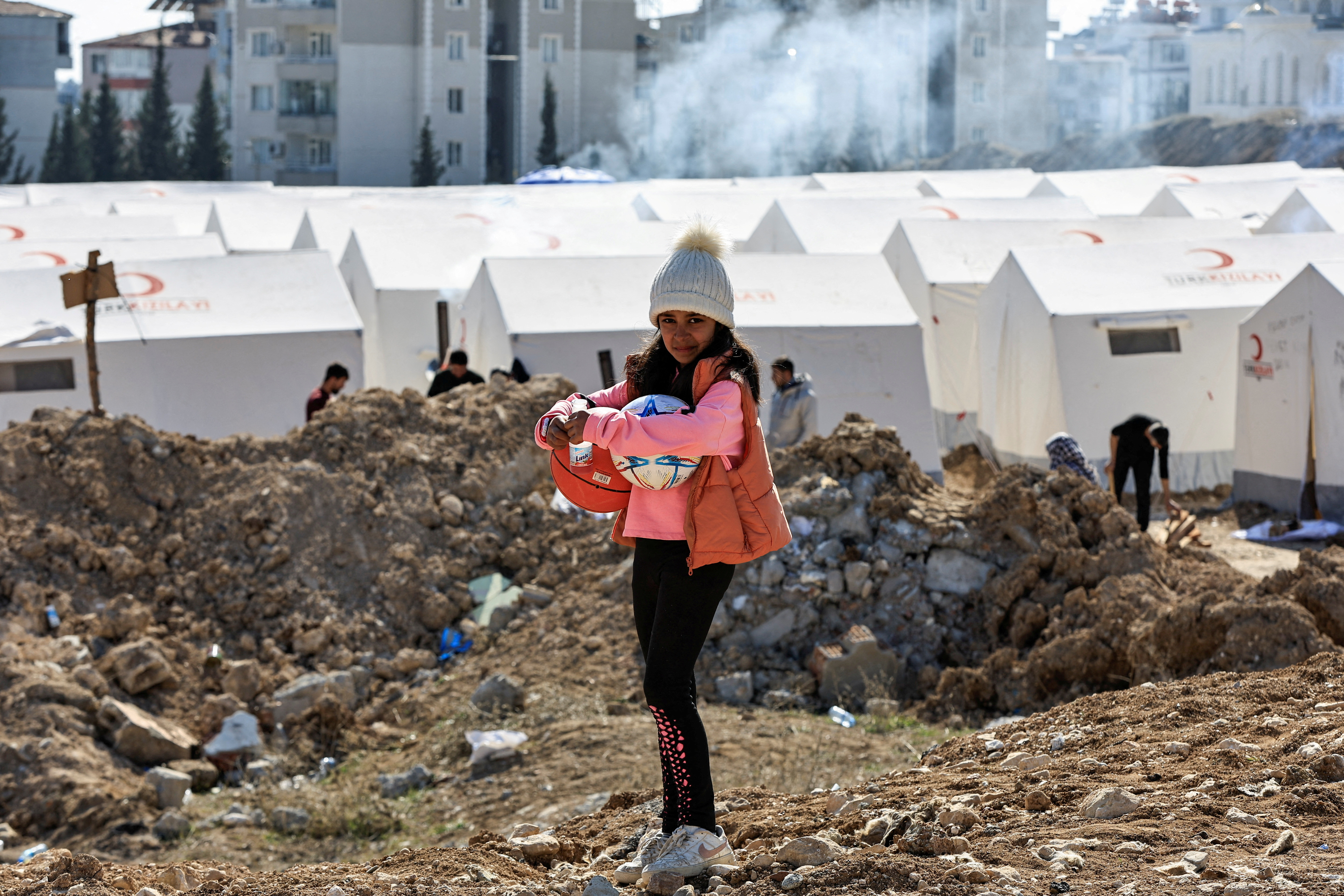 A girl holding sports balls stands at a camp for survivors, in the aftermath of the deadly earthquake, in Adiyaman, Turkey February 18, 2023