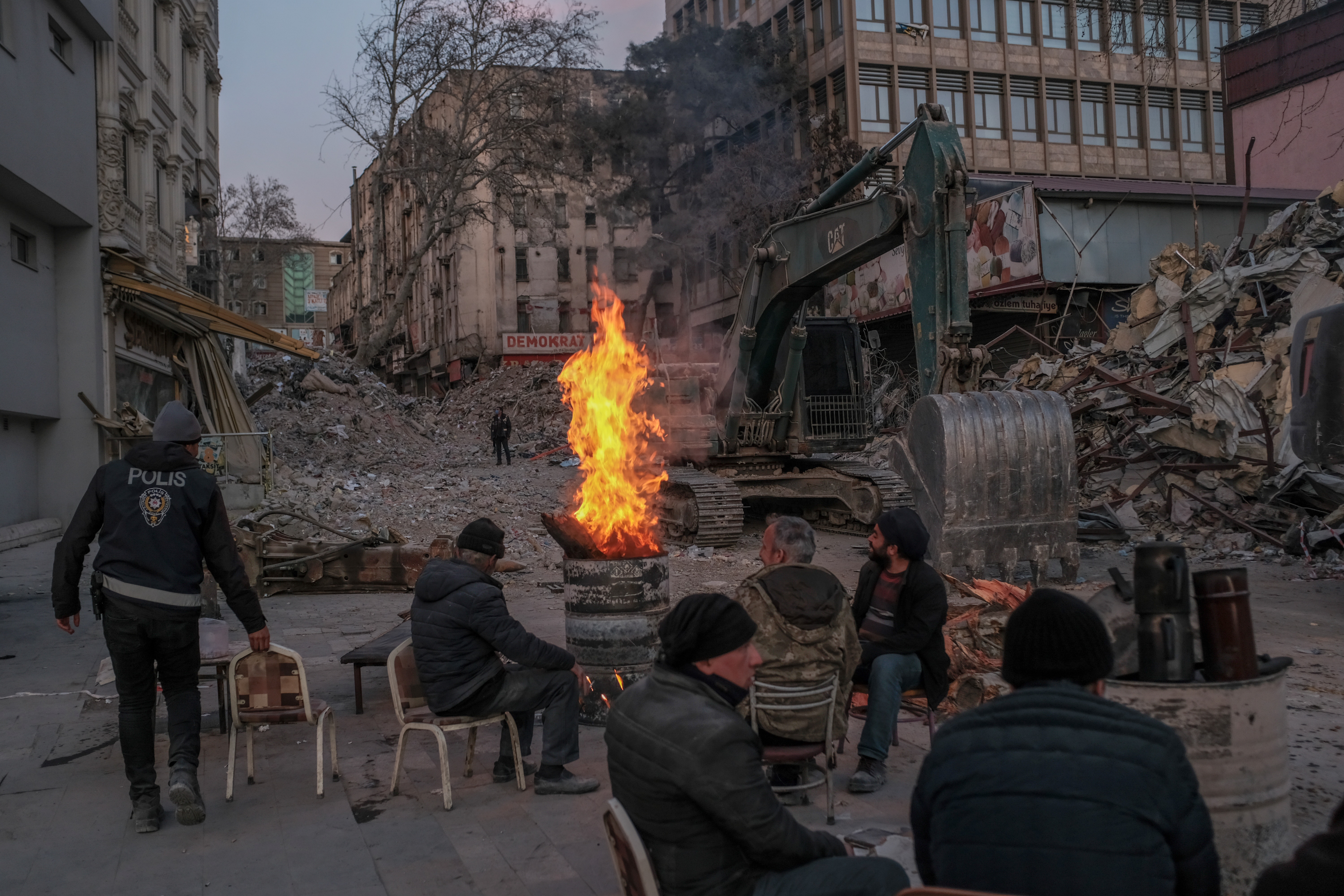 People warm up next to a fire as they take a break from working on removing rubble of collapsed buildings
