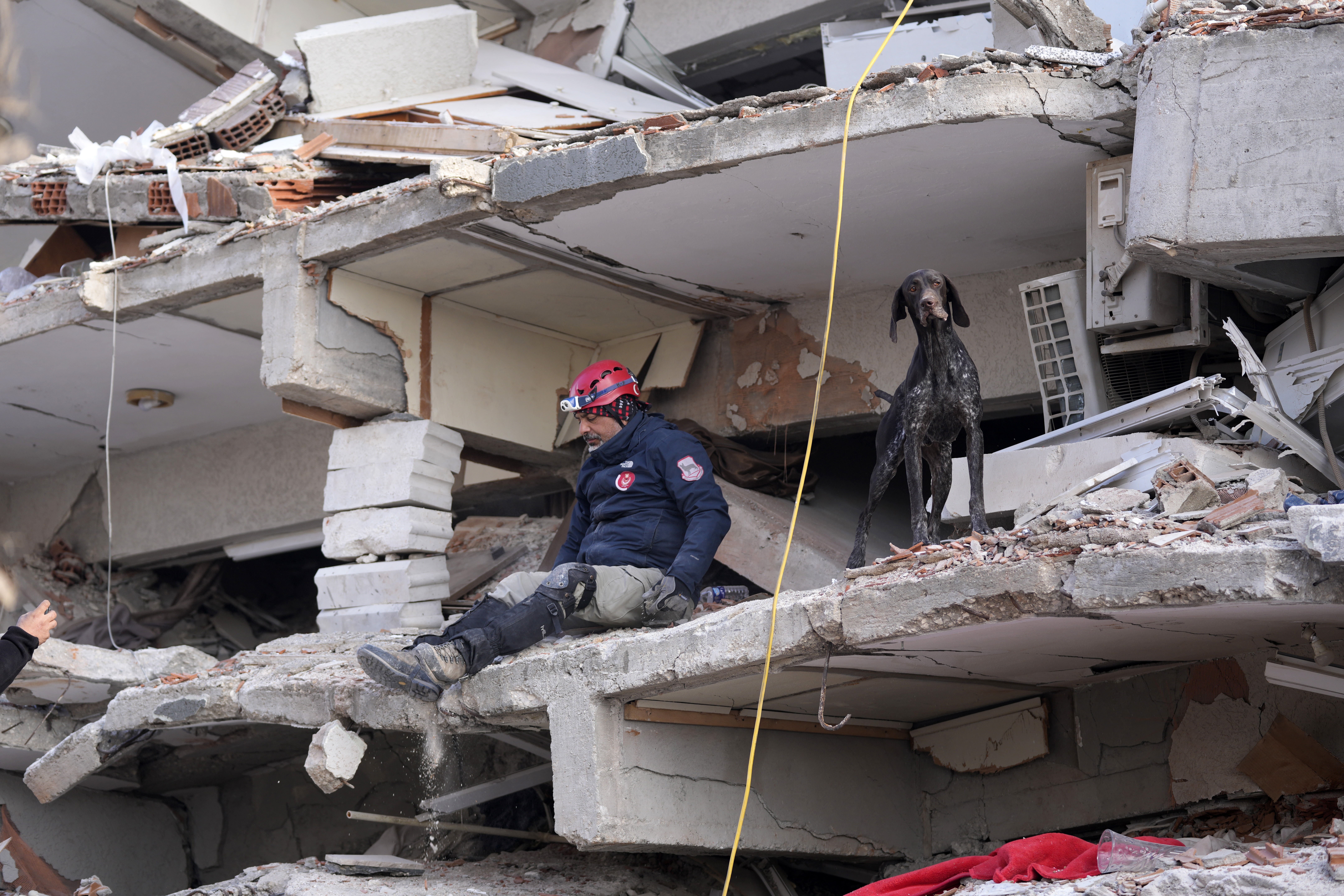 A rescuer with a sniffer dog searches in a destroyed building in Antakya, southeastern Turkey, Friday, Feb. 10, 2023. Rescuers pulled several earthquake survivors from the shattered remnants of buildings Friday, including some who lasted more than 100 hours trapped under crushed concrete after the disaster slammed Turkey and Syria. (AP Photo/Hussein Malla)
