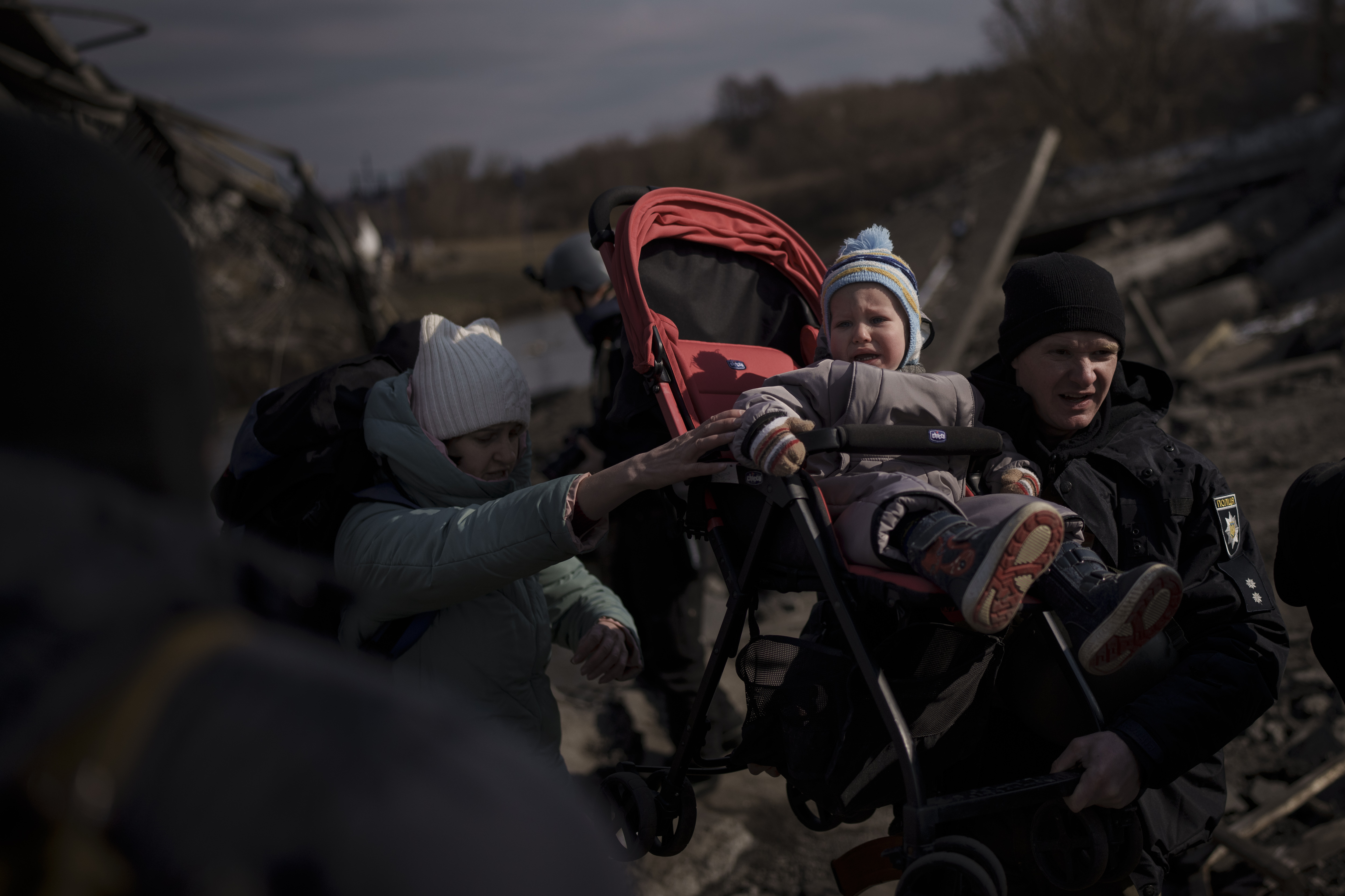 A child in a stroller is lifted across an improvised path as people flee Irpin, on the outskirts of Kyiv