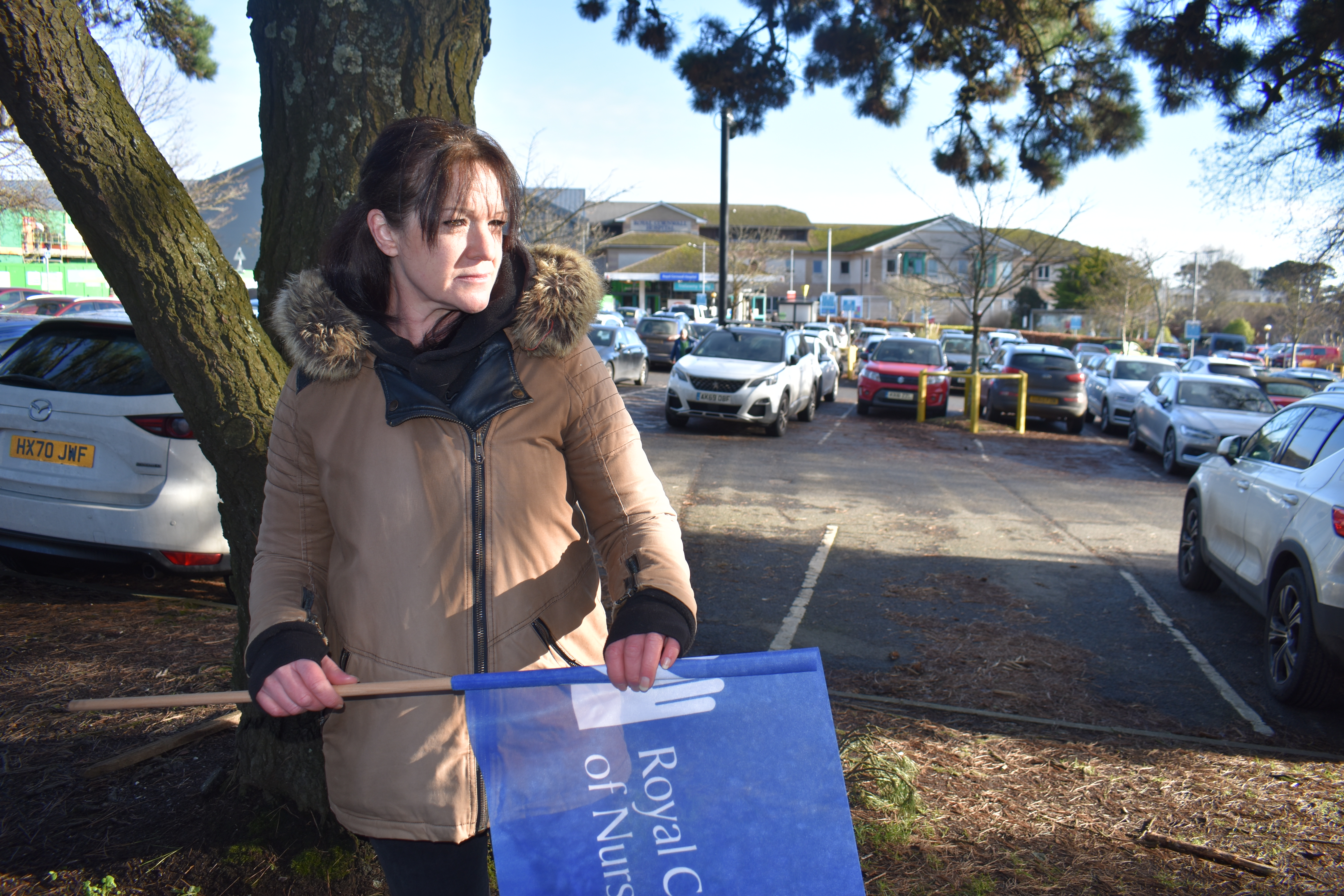 A photo of a person holding a Royal College of Nursing flag with a parking lot in the background.