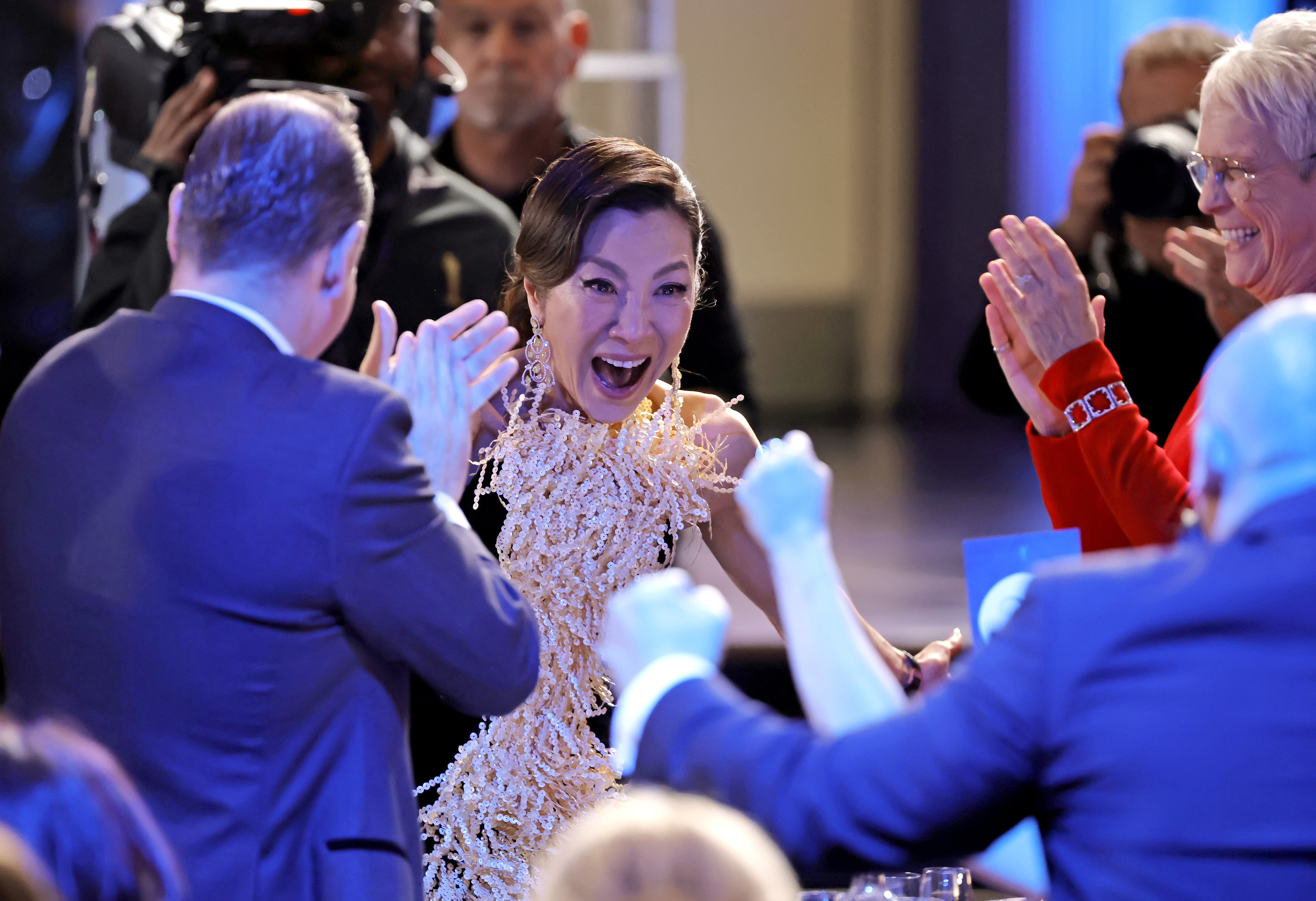 Michelle Yeoh pictured as she heard she had won best actress. She looks thrilled. People around her are punching the air and clapping.